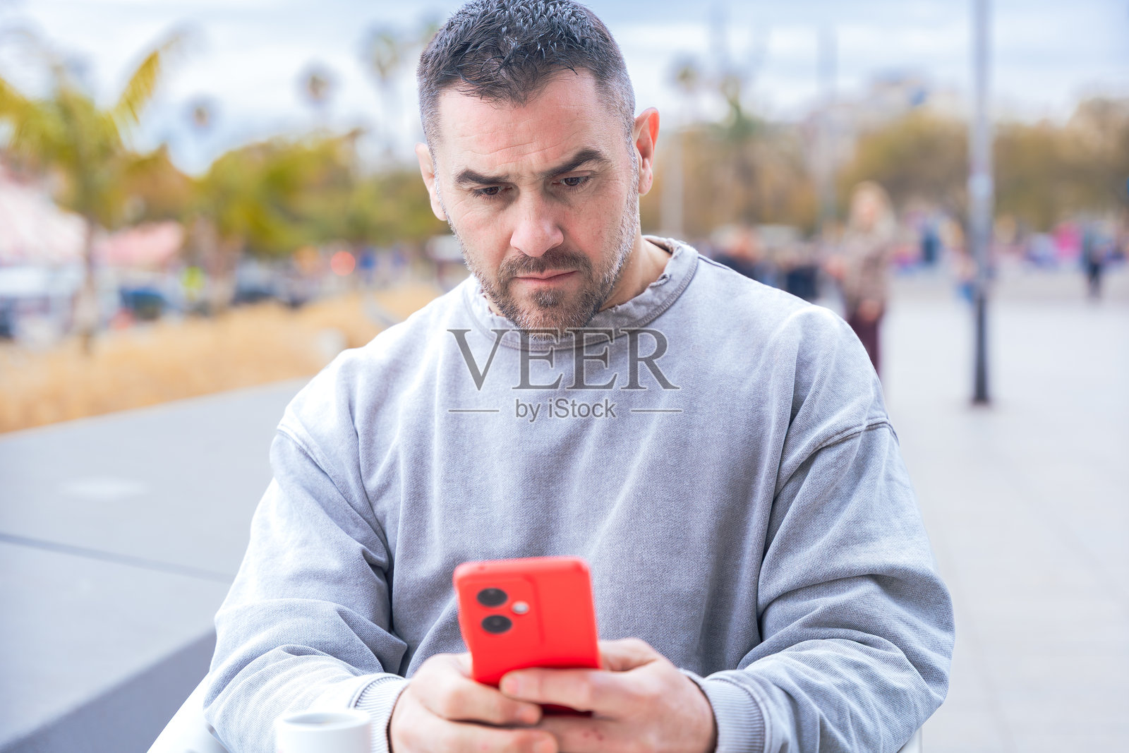 在户外咖啡馆里，一位严肃的男子认真地用智能手机打字。照片摄影图片