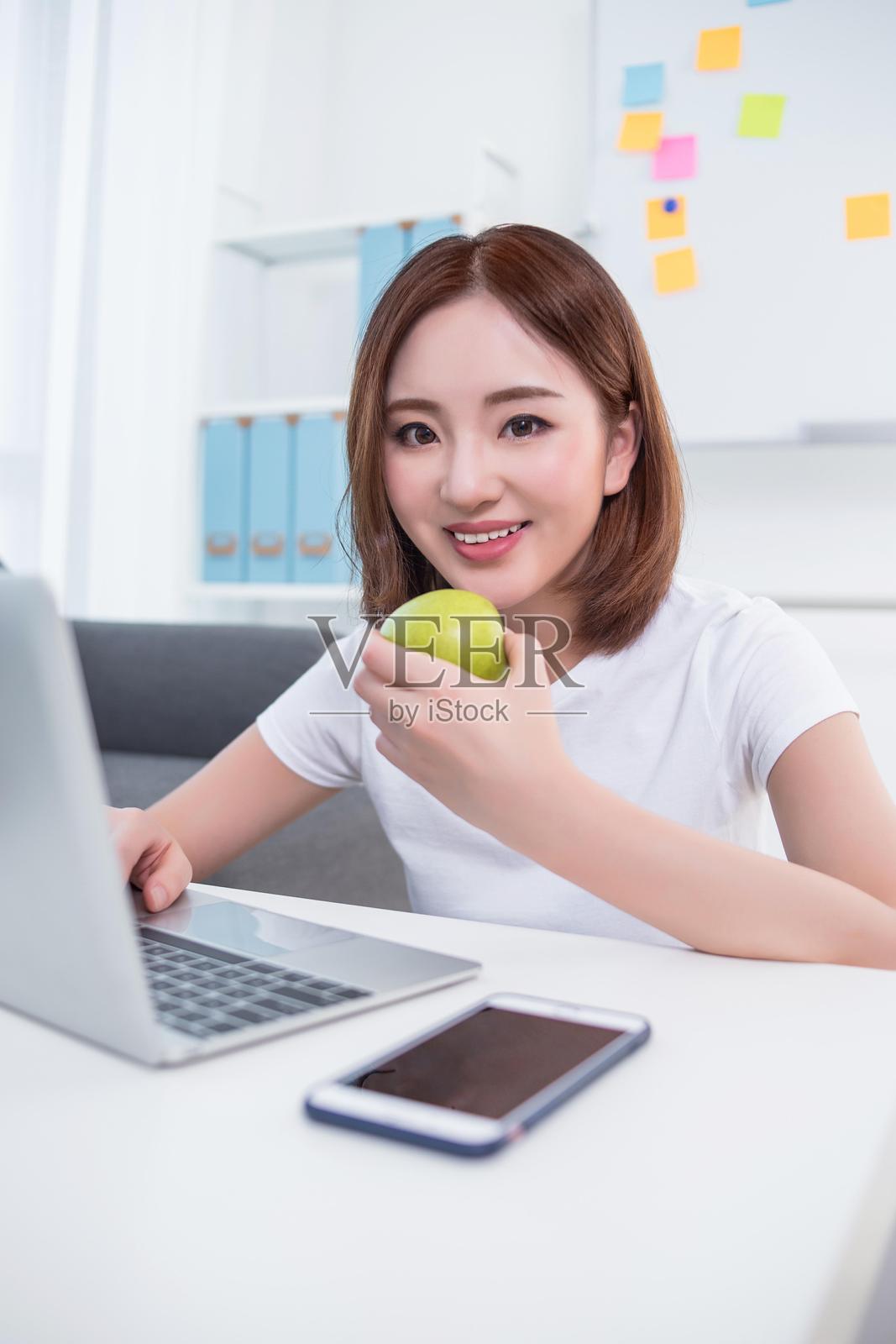 女性在使用笔记本电脑时吃苹果照片摄影图片