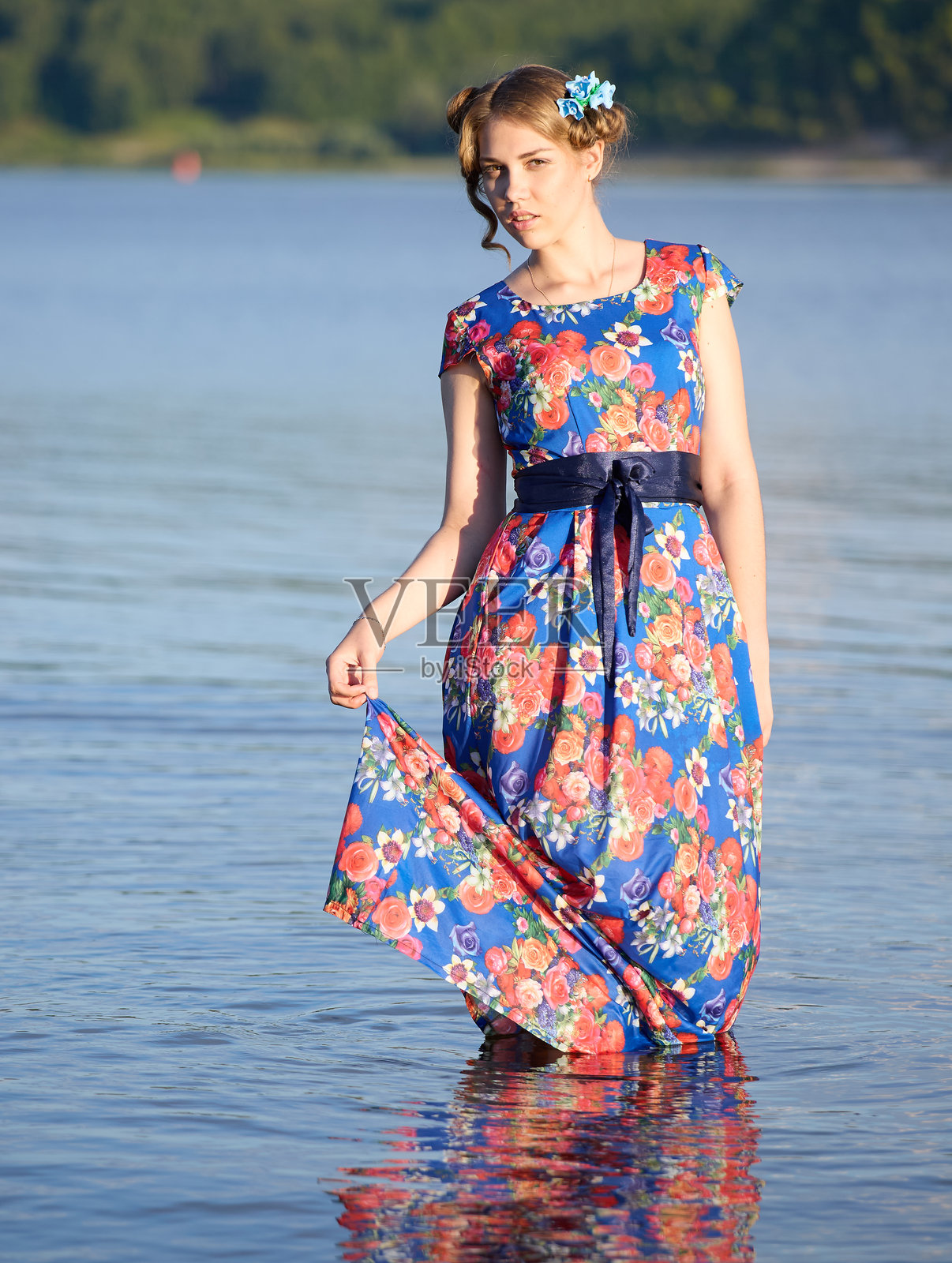 一个美丽的女孩站在河边，手握阳光裙的下摆，若有所思地看着镜头。照片摄影图片