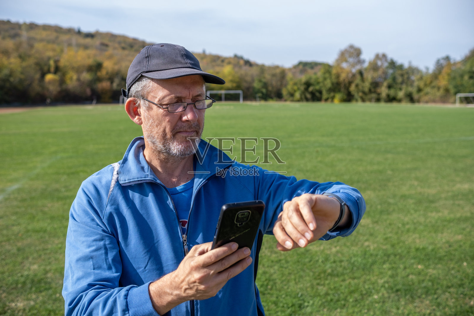 一个男人在绿色运动场上查看他的运动手环和手机。照片摄影图片
