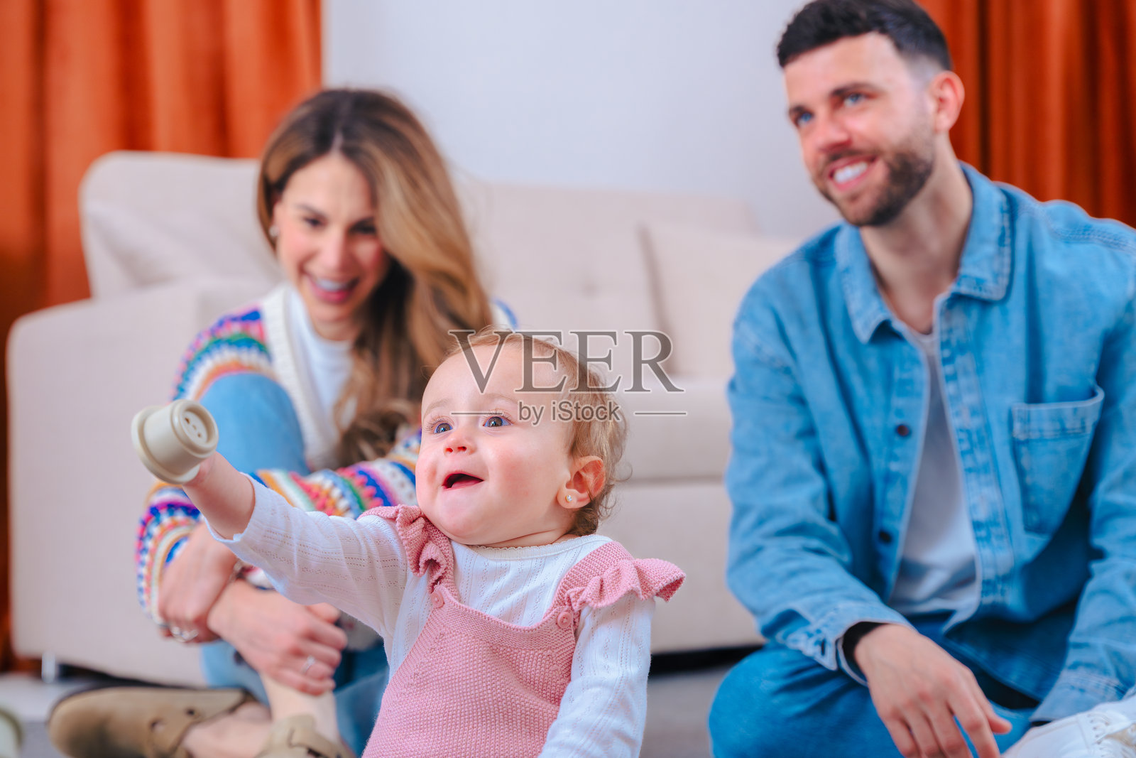 父母在地毯上鼓励穿着粉色工装的女孩享受快乐的家庭时光。照片摄影图片