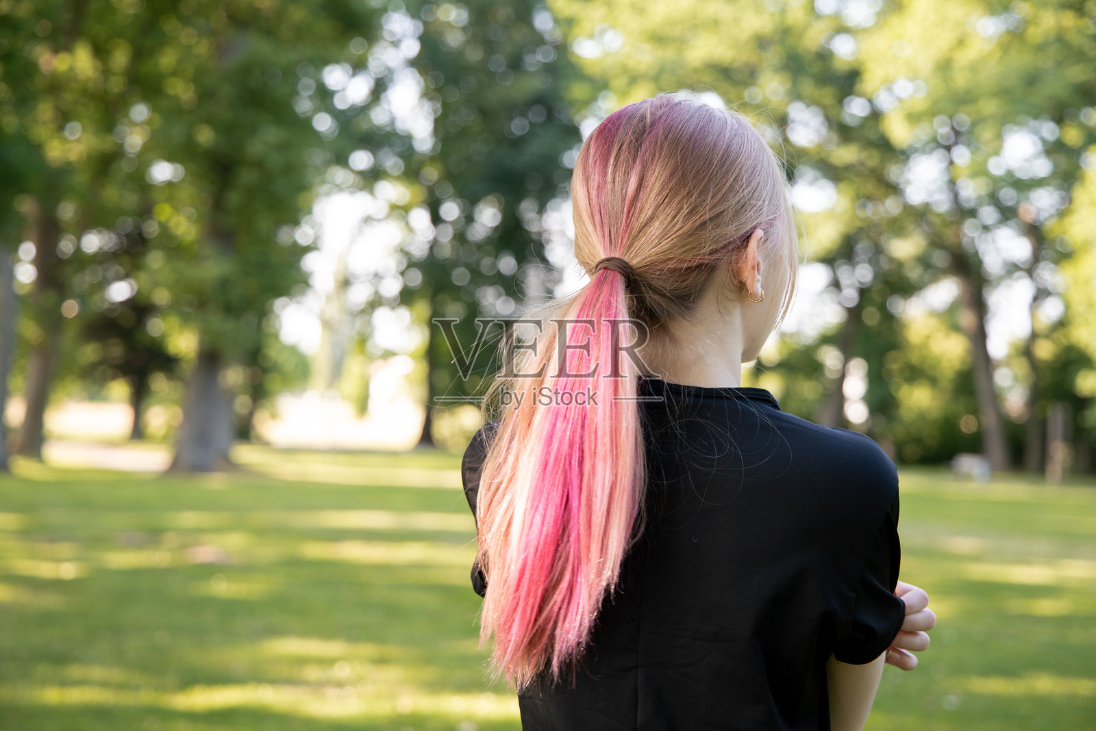 年轻女子在郁郁葱葱的公园里站着，享受着阳光明媚的日子，周围是树木和大自然的宁静。照片摄影图片