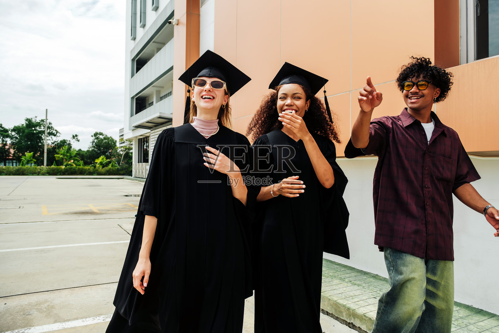 三位快乐的年轻毕业生在毕业典礼后分享欢笑与兴奋。他们身穿学士服和学位帽，在户外庆祝成功与友谊，享受轻松愉快的时刻。照片摄影图片