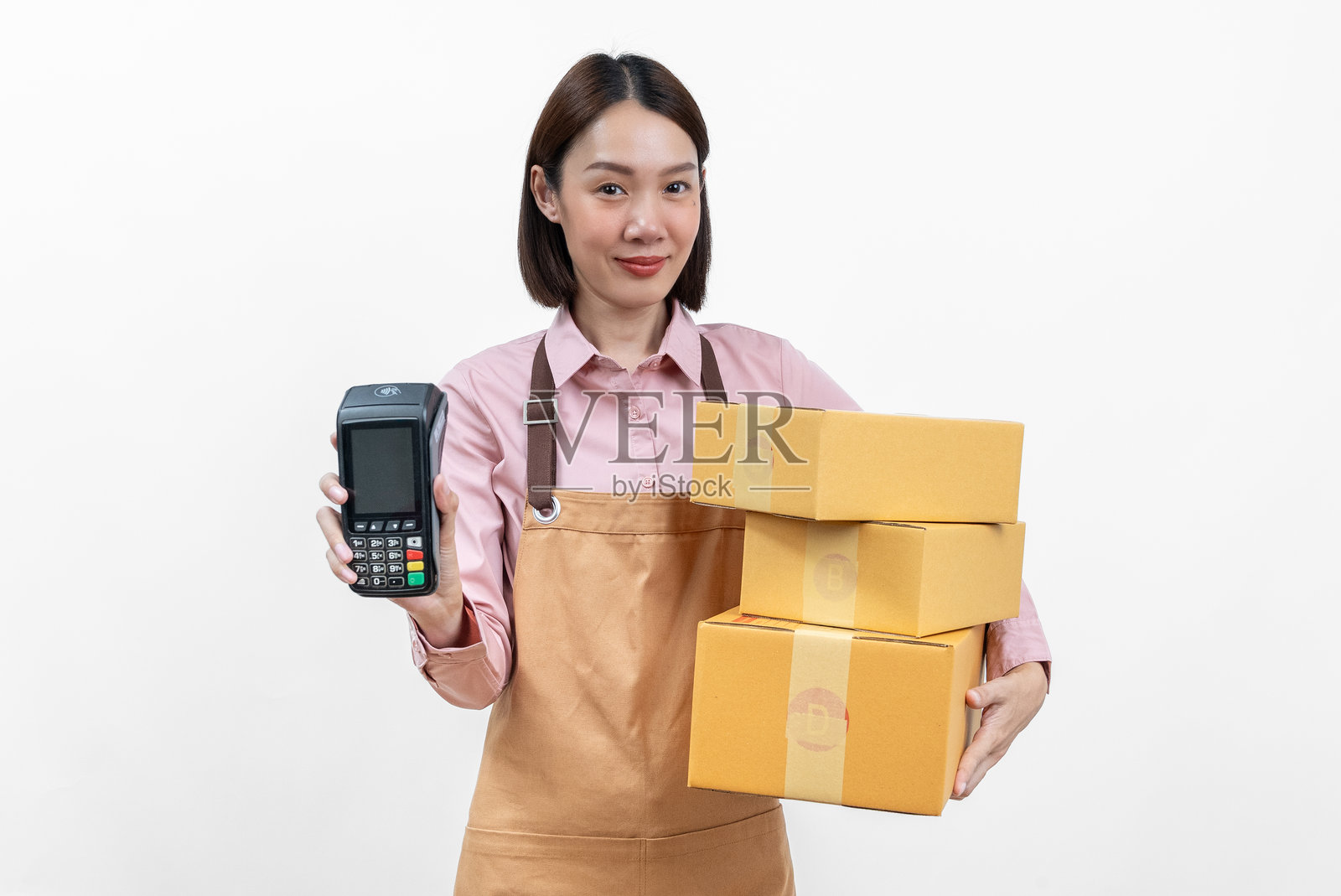美丽的亚洲女性企业主与箱子和电子支付终端或信用卡终端合影，背景为纯白色。在线购物时输入信用卡的序列号进行支付。照片摄影图片