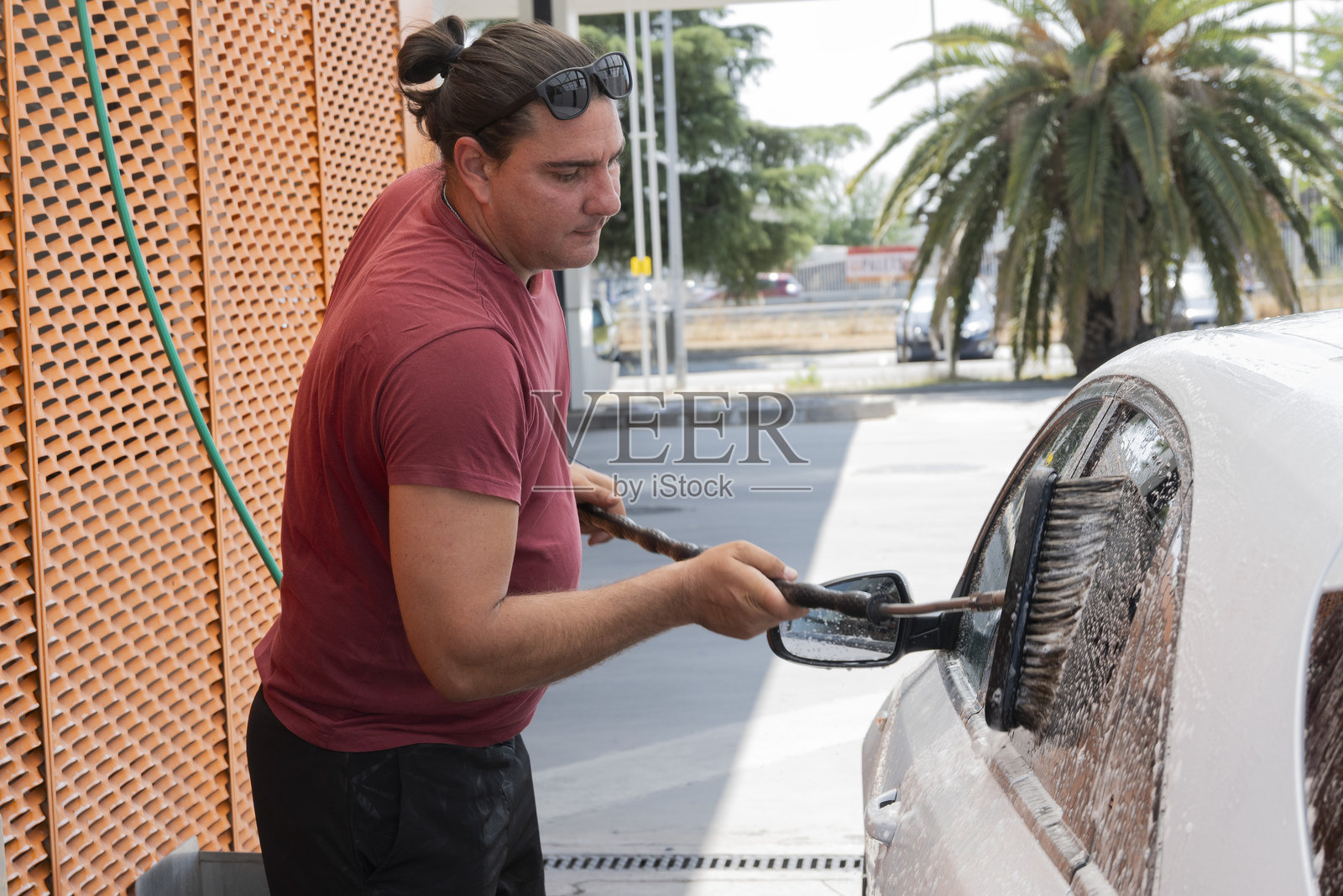 男子在自助洗车场用刷子和肥皂清洗汽车窗户照片摄影图片