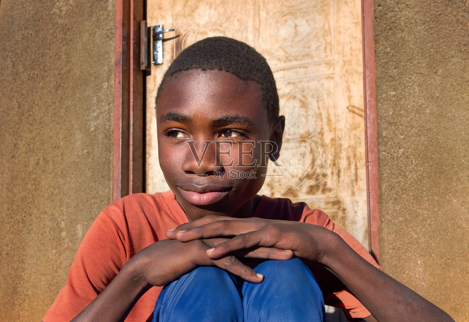 村庄里一个非洲年轻男孩，坐在房子前的院子里，阳光明媚。照片摄影图片