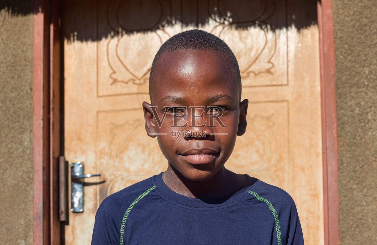 村庄里一个非洲小男孩坐在房子前的院子里，面带微笑。照片摄影图片