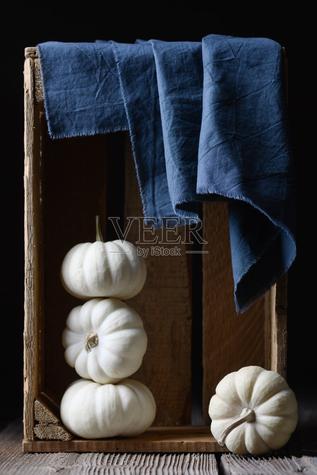 白色装饰性的小南瓜放在木箱里，旁边有蓝色餐巾。照片摄影图片