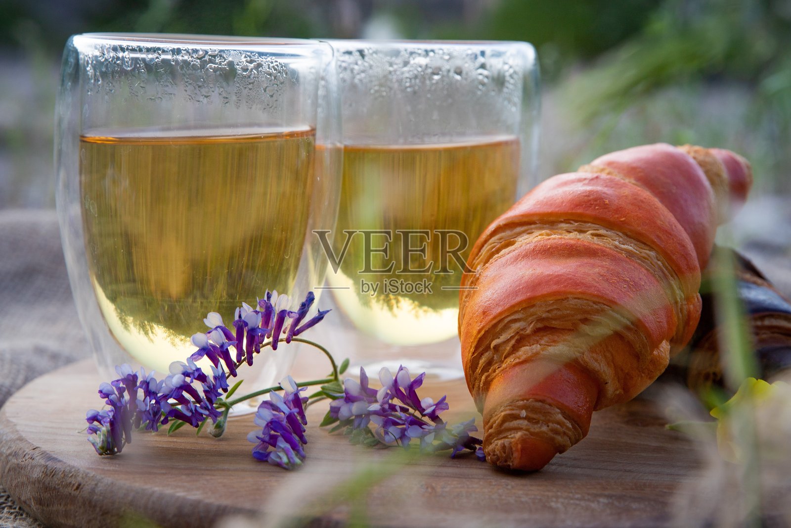 户外野餐，木托盘上摆放着茶、可颂和野花照片摄影图片