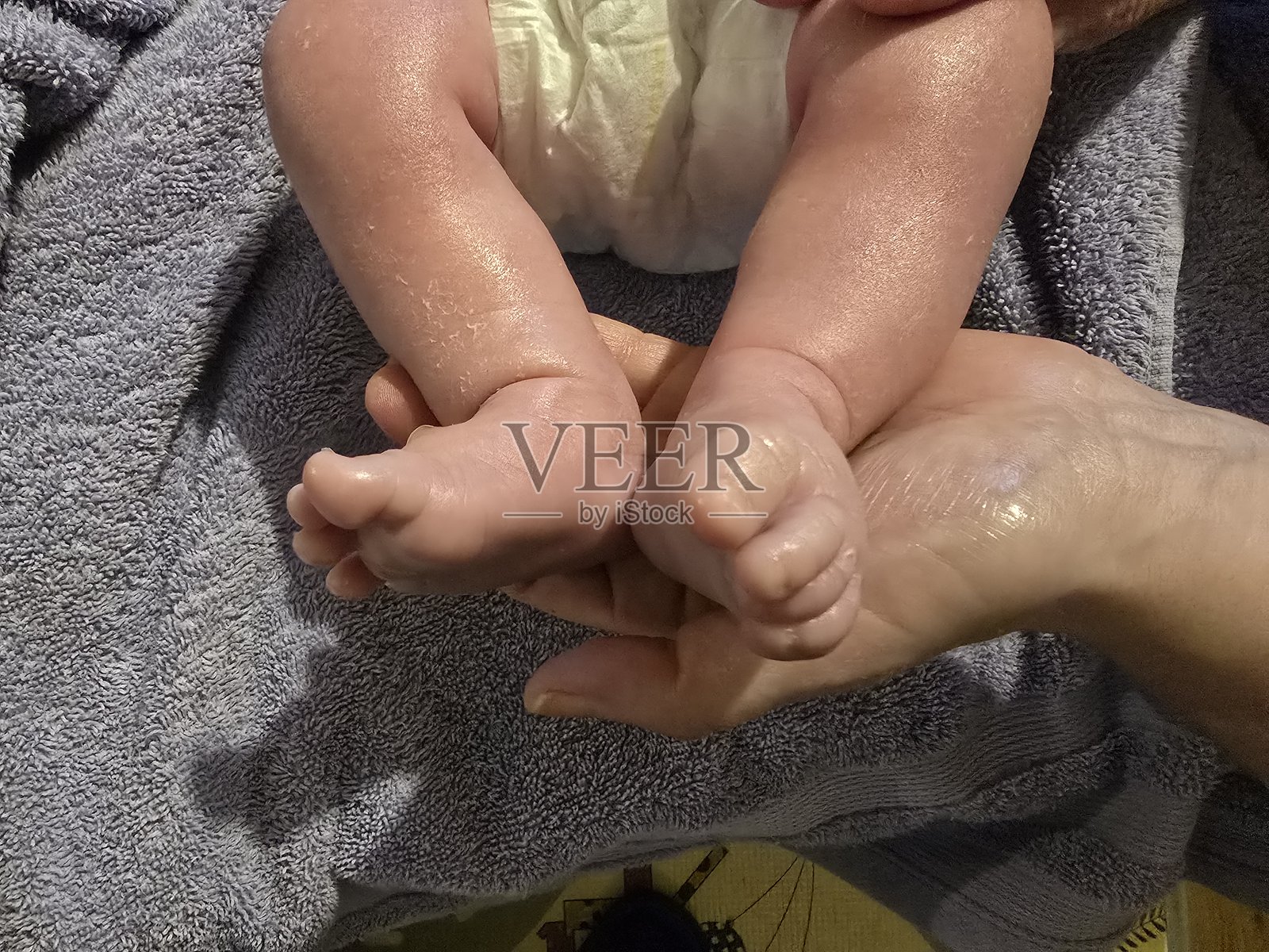 一双小婴儿的脚被轻轻地托在成年人的手中，放在灰色毛巾上，展现出新生肌肤的细腻纹理。照片摄影图片
