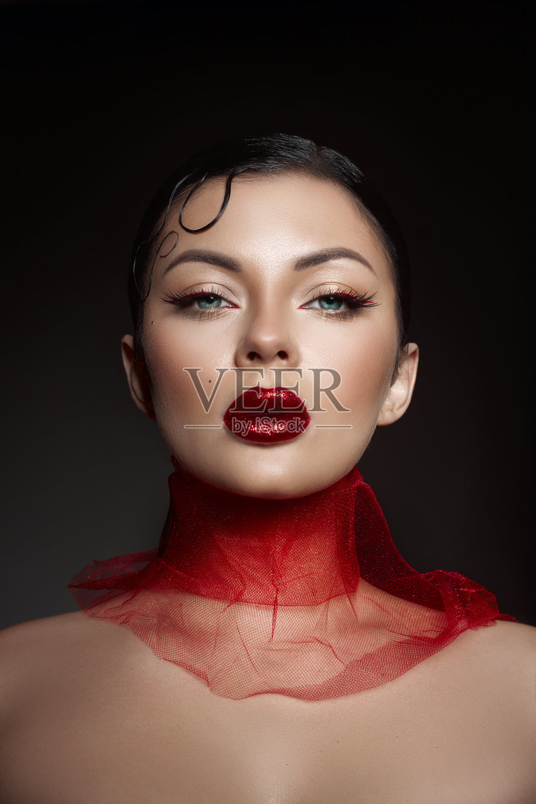 自信的模特摆姿势，展示光泽红唇和戏剧性的眼妆。光滑的发型与她脖子周围的透明红色面料相得益彰，营造出大胆而迷人的外观。照片摄影图片