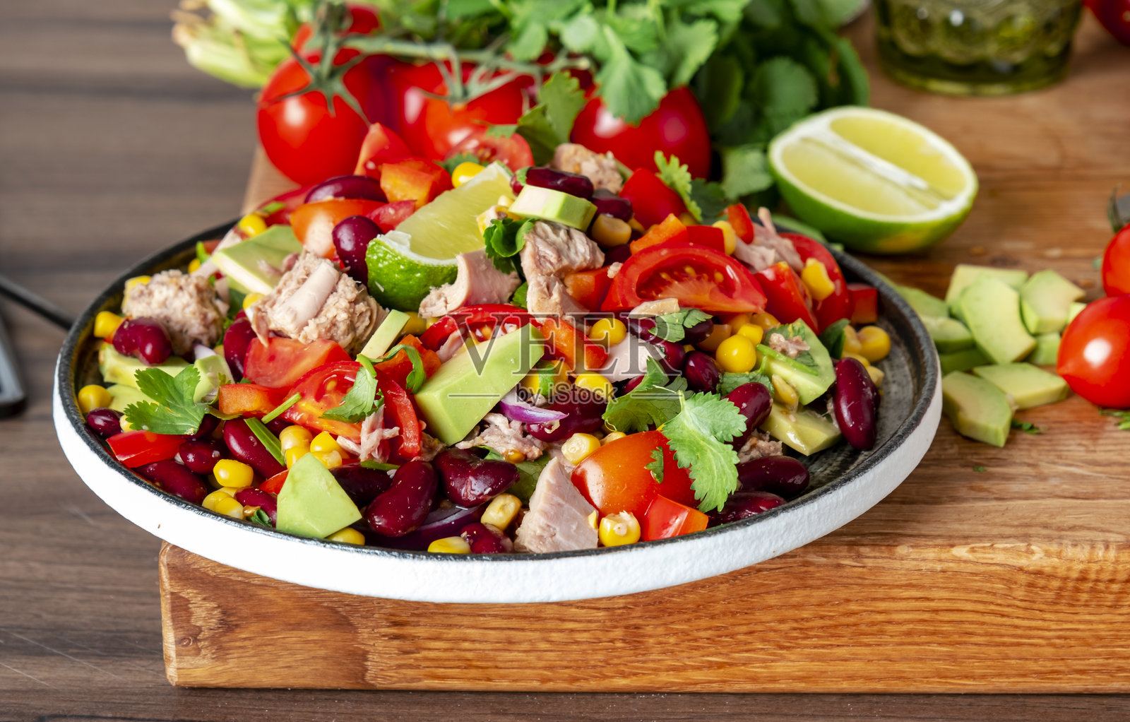在厨房台面上准备美味的沙拉，配料有金枪鱼、玉米、鳄梨、豆类、西红柿和香菜，旁边的木砧板上放着准备食材。照片摄影图片