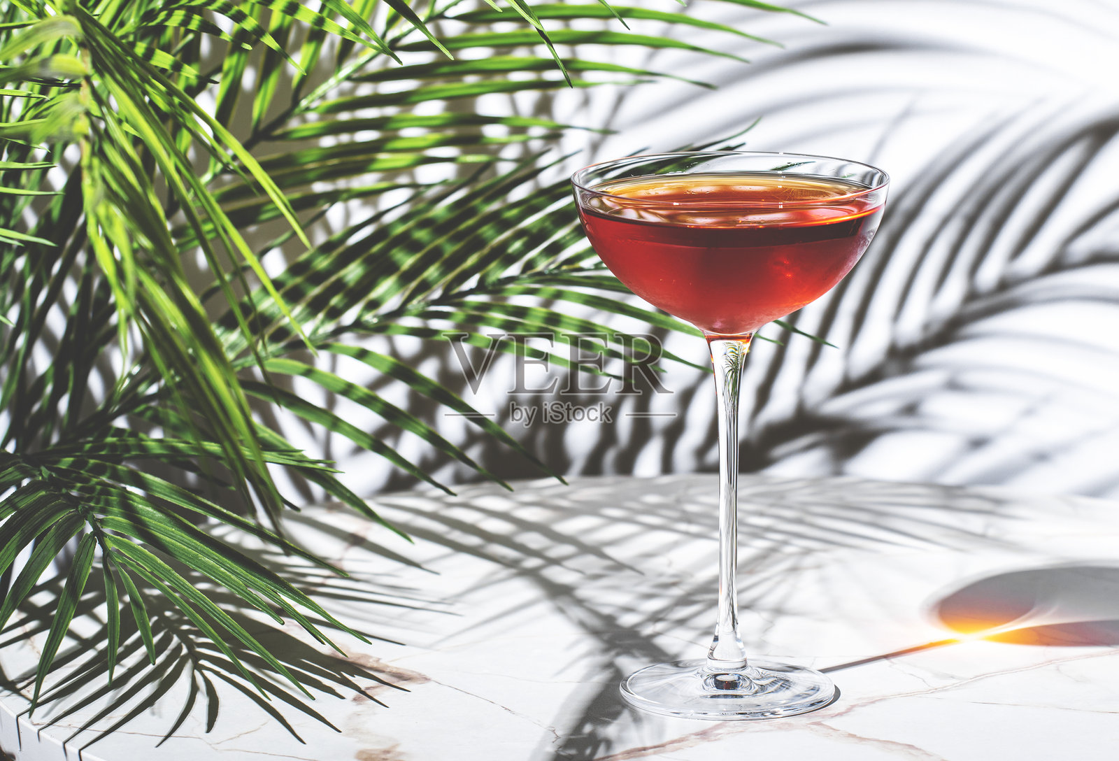鲜艳的红色鸡尾酒，含有威士忌、波特酒、苦味酒和苦精，优雅地放置在大理石桌上，周围环绕着棕榈叶。照片摄影图片