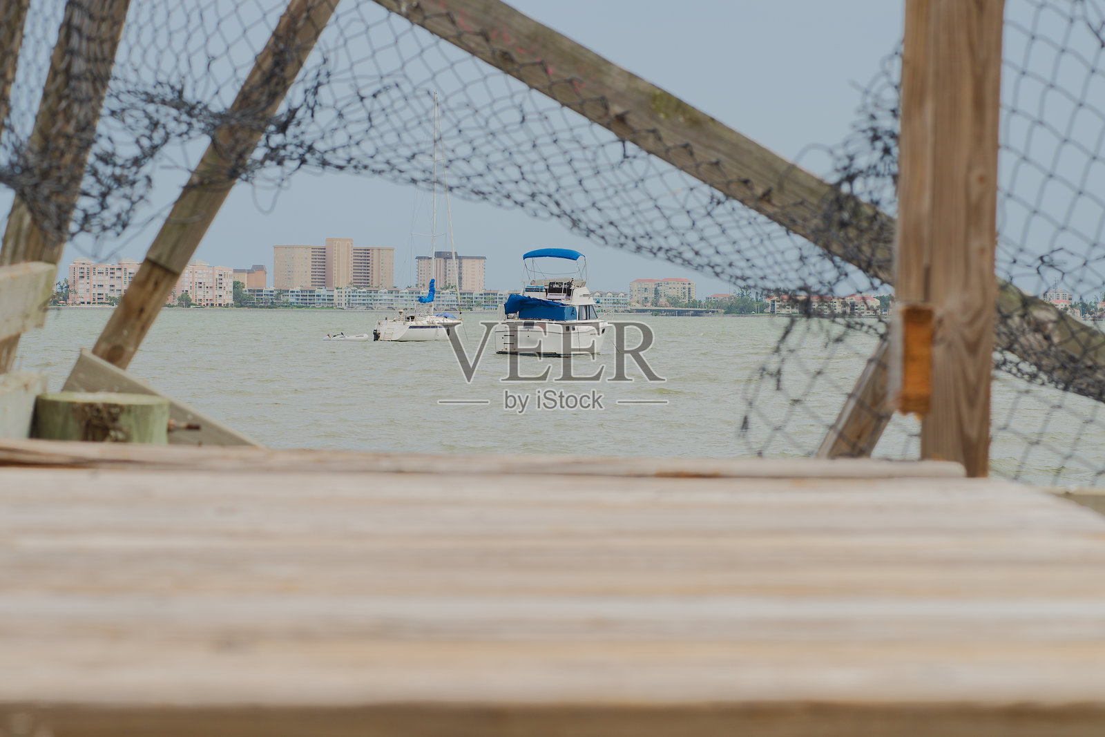 宁静的水边，船只与城市景观被破损的木栈道和渔网框住，佛罗里达州古尔夫波特照片摄影图片