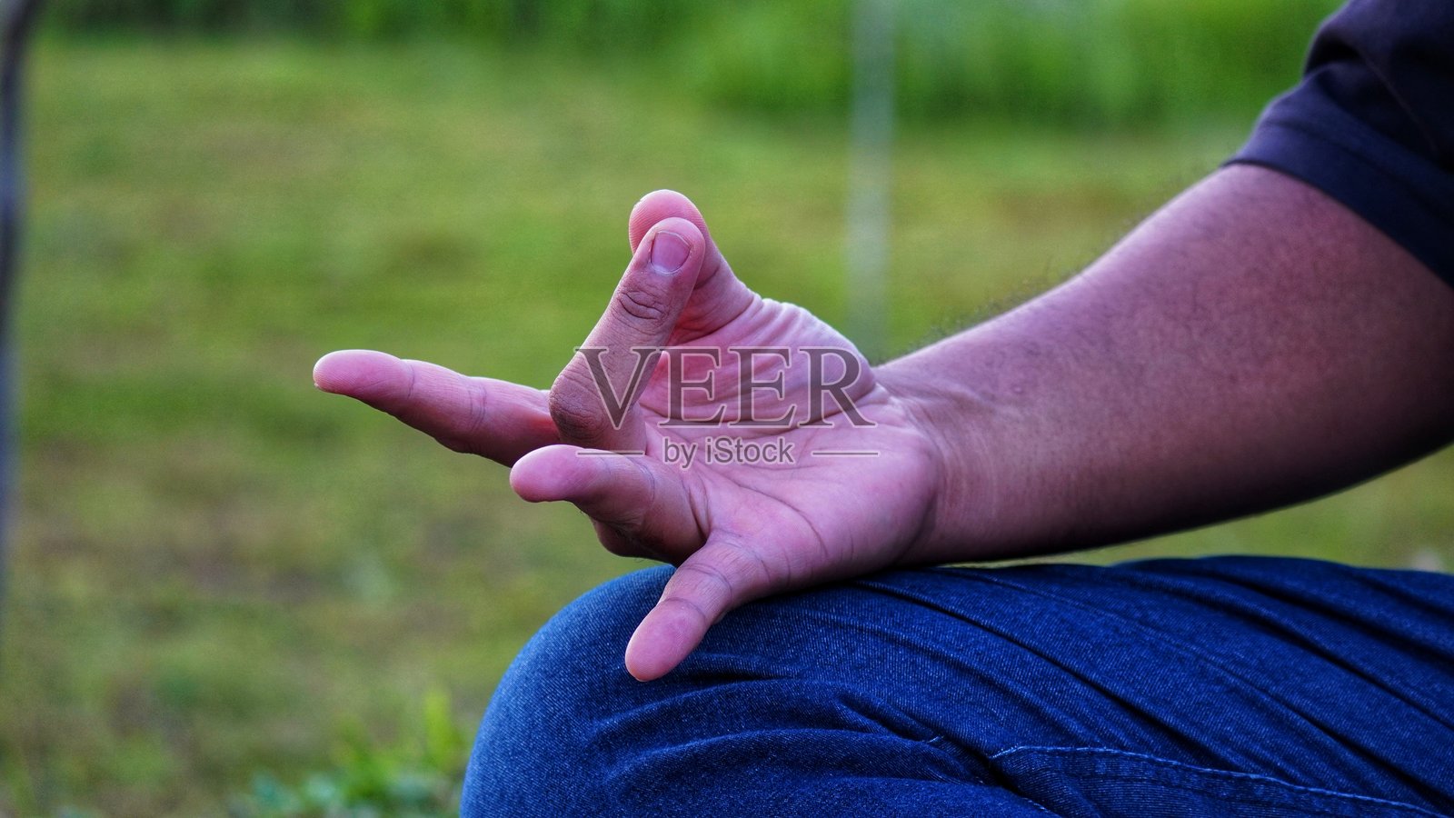一只手展示瑜伽或冥想的手势，背景模糊且呈绿色。照片摄影图片