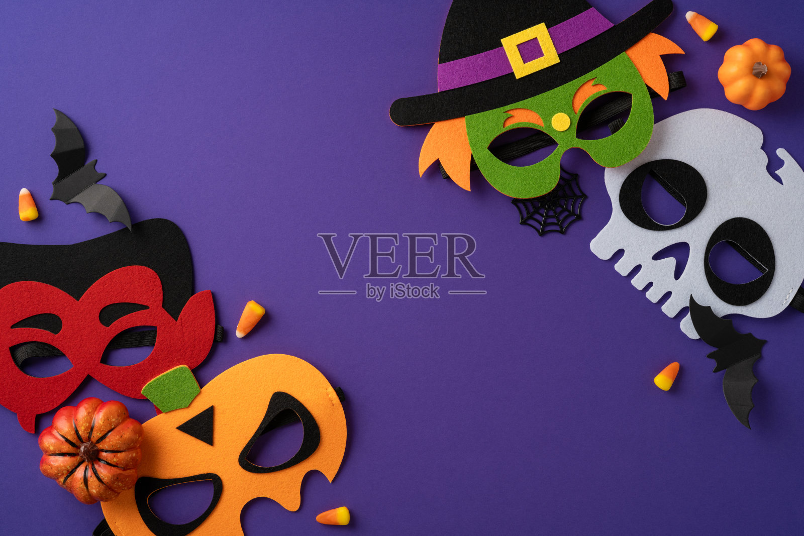 装饰性的万圣节面具与季节性元素和糖果摆放在紫色背景上照片摄影图片