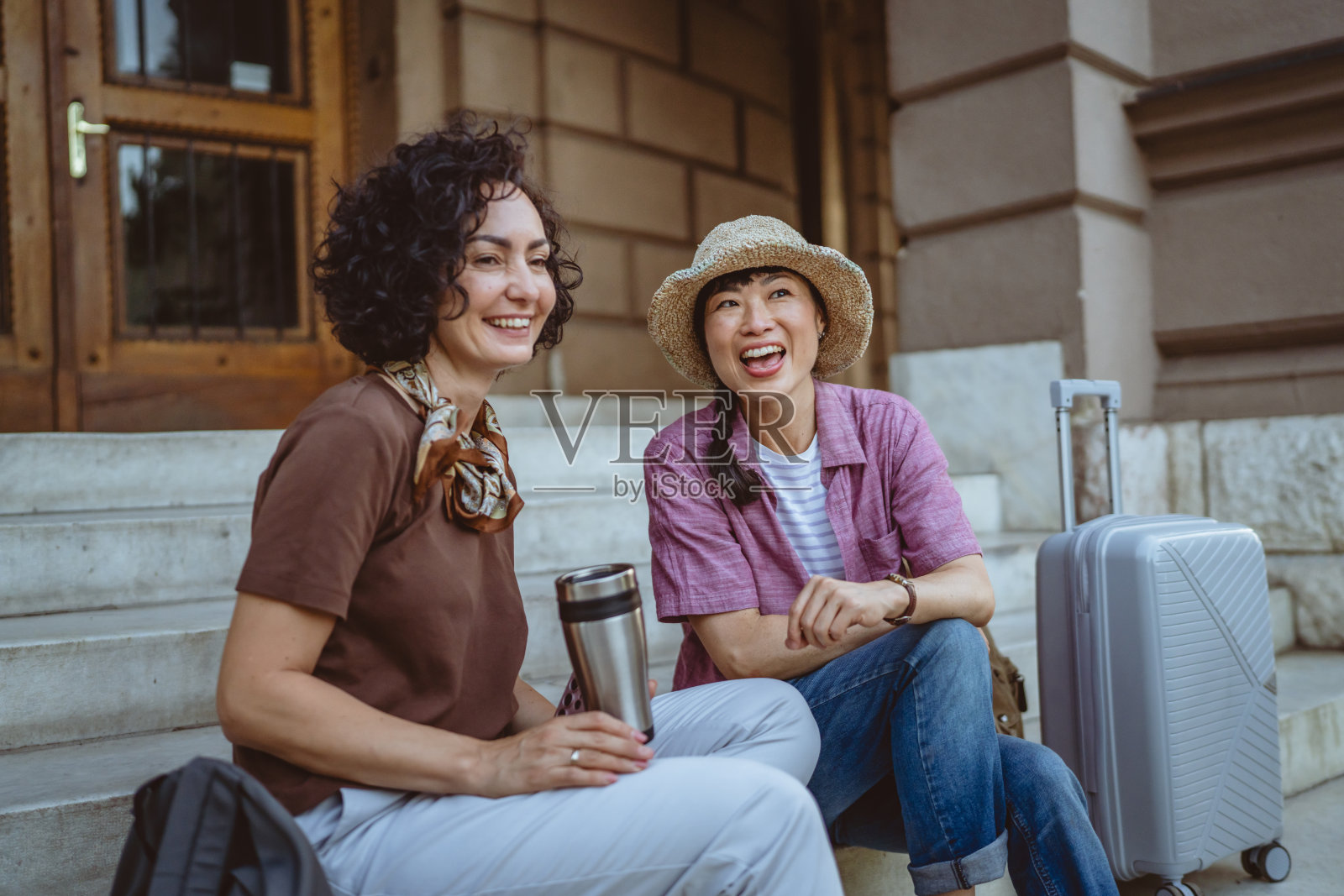 两个女性游客朋友在楼梯上讨论，手里提着行李箱。照片摄影图片