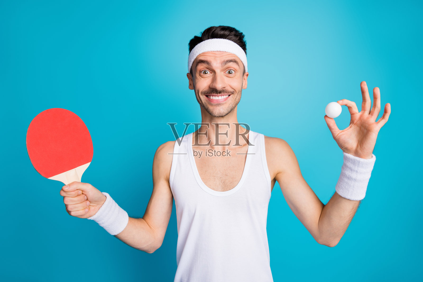 年轻运动员开心地微笑，手持乒乓球和球拍，背景为蓝色。照片摄影图片