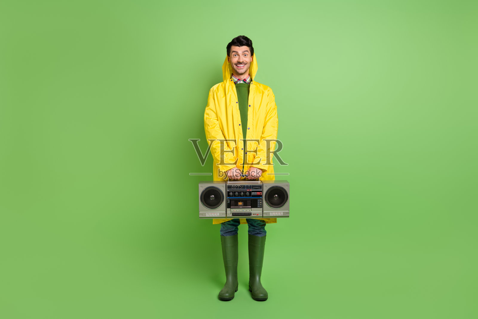 全身照，年轻快乐积极的帅气男士穿着外套，手持音响，背景为绿色。照片摄影图片