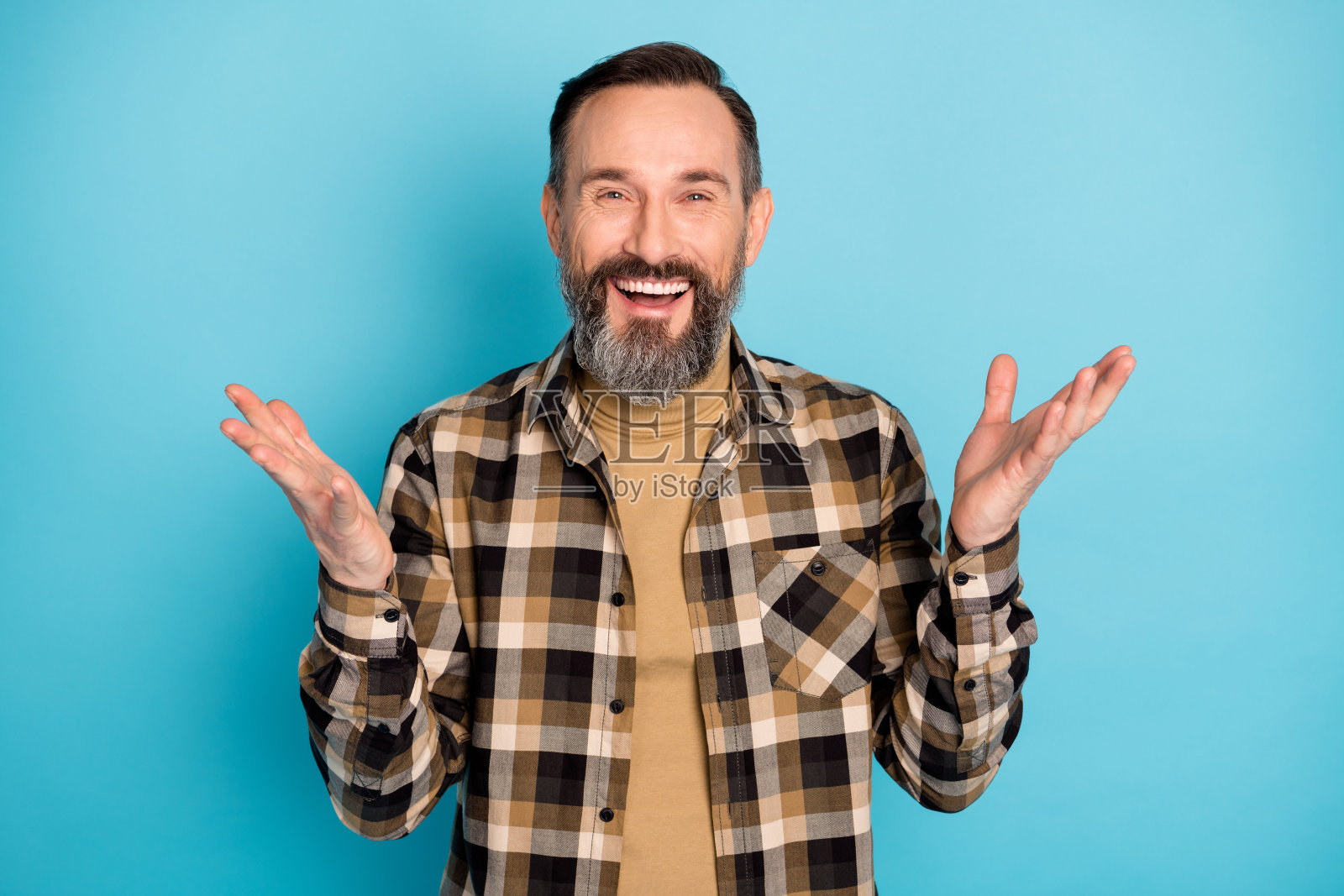快乐的老年男子在鲜艳的蓝色背景下笑着，手势夸张，似乎在讲一个有趣的笑话。照片摄影图片
