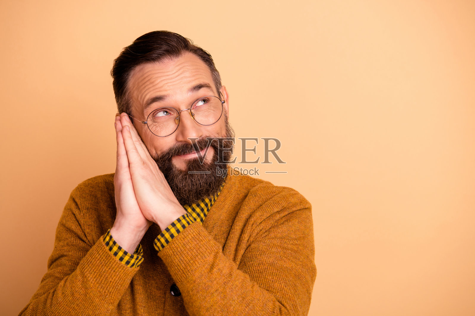 梦幻般的男子睡觉，双手放在脸下，目光空洞，穿着毛衣，背景为米色。照片摄影图片