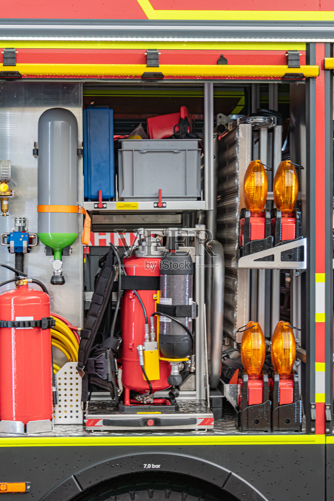 消防车的开放舱室展示了消防设备、软管、喷嘴、连接器和氧气罐，黄色灯光可见，真实风格，重点在设备上。照片摄影图片