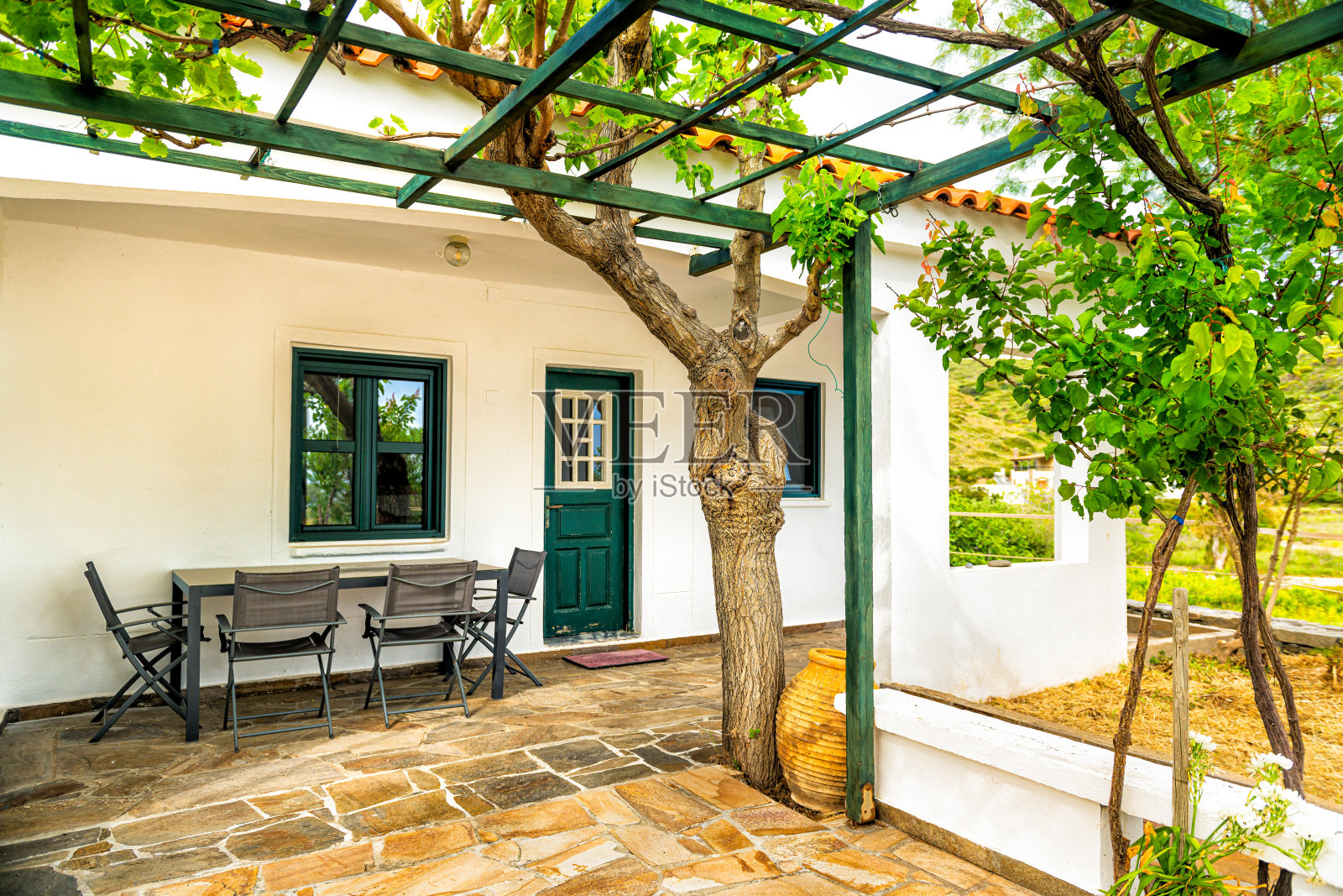 希腊伊卡里亚岛的家居庭院，户外餐桌，椅子旁的藤架凉亭，夏季的葡萄和杏树照片摄影图片