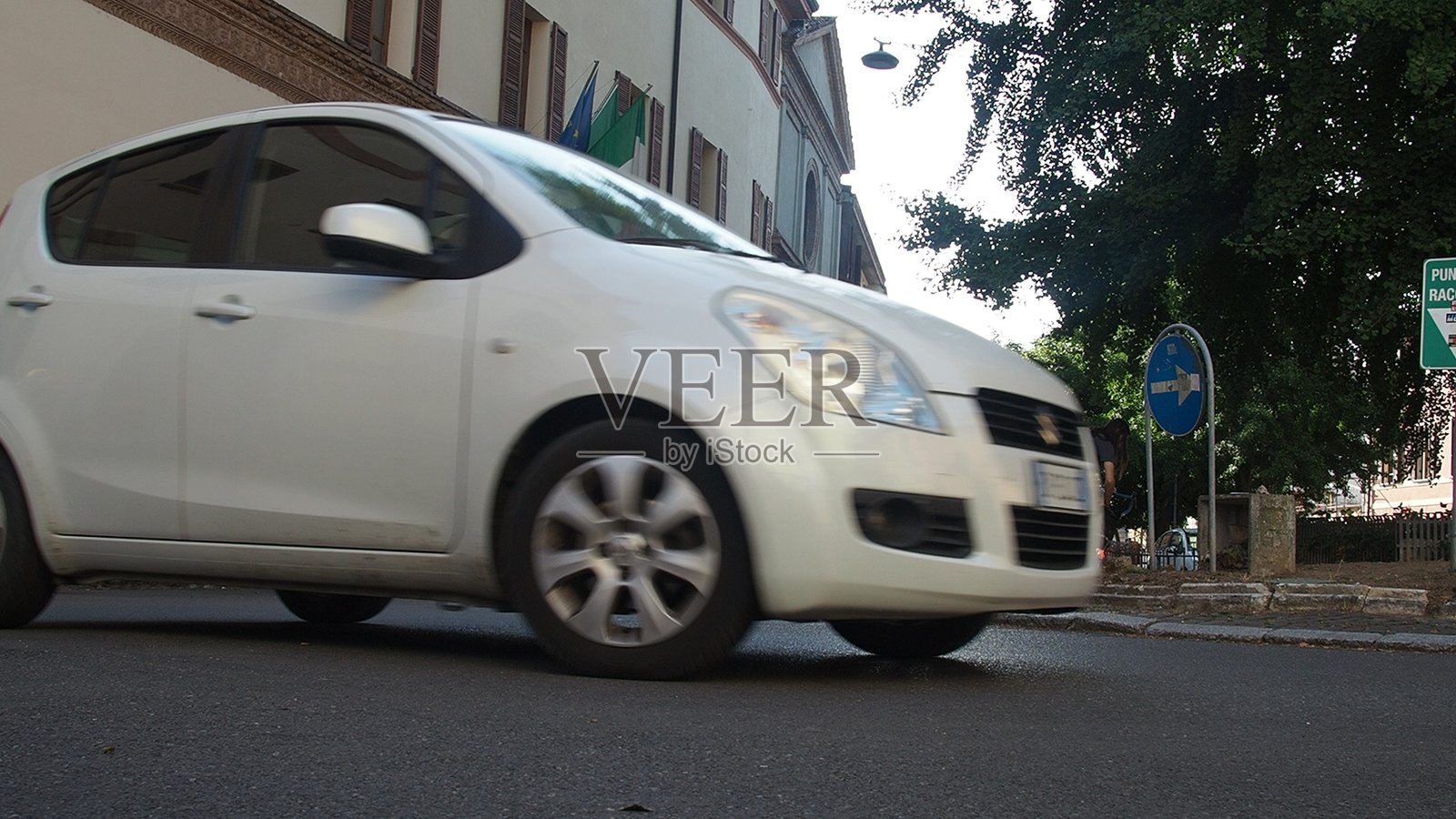 一辆白色城市汽车在意大利克雷莫纳的阳光明媚的街道上行驶，展示了当地的城市交通和欧洲建筑，正值温暖的夏日白天。照片摄影图片