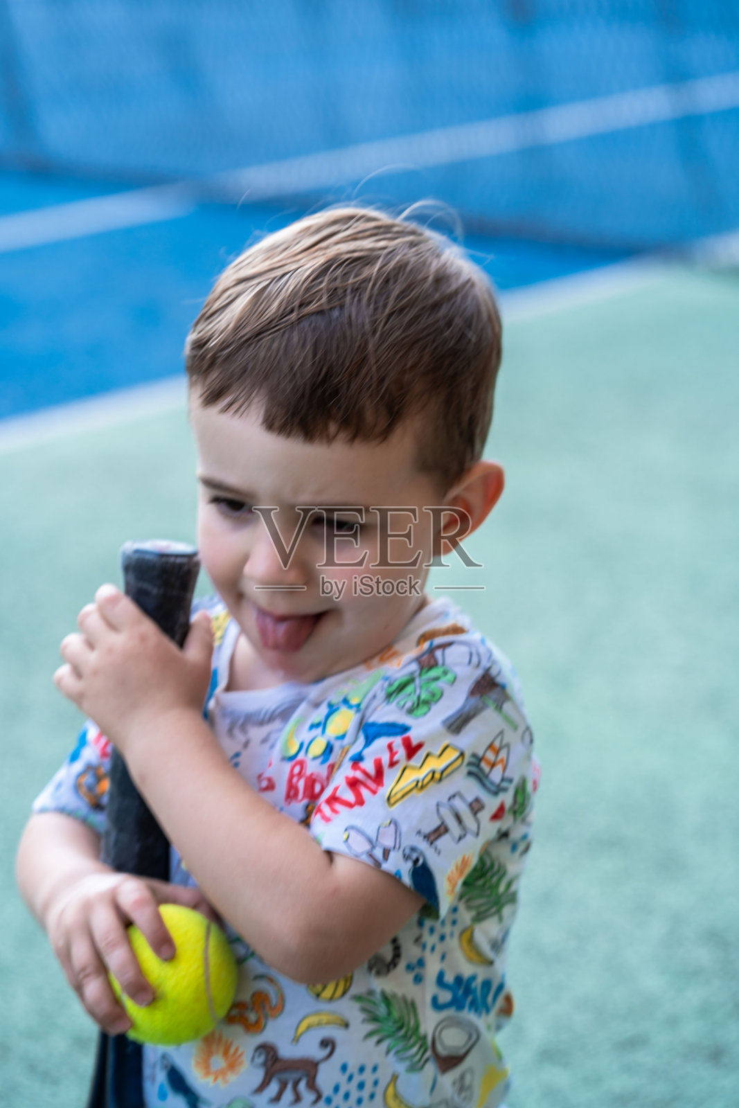 孩子在乒乓球场上打网球，吐着舌头。照片摄影图片