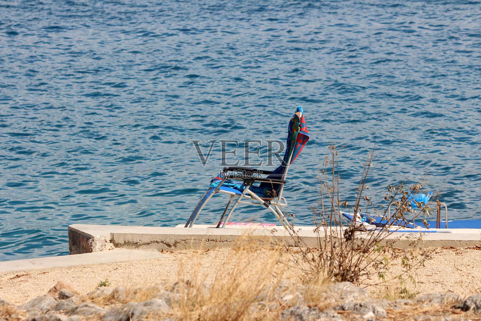 孤独的海滩椅面朝宁静的蓝色海洋，位于混凝土码头上照片摄影图片