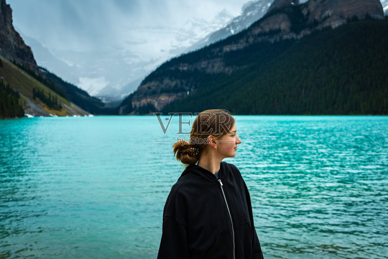 穿着黑色连帽衫的女人站在碧绿色湖边照片摄影图片