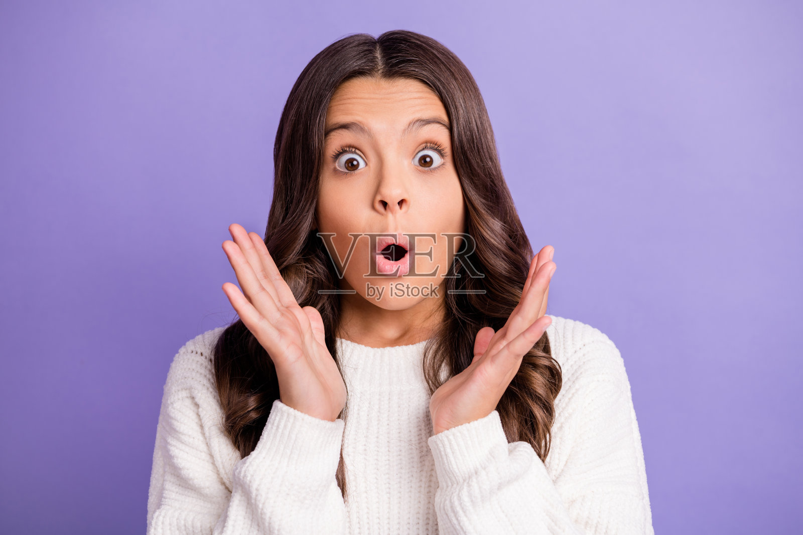 年轻美丽的女孩惊讶地盯着镜头，背景为紫色。照片摄影图片