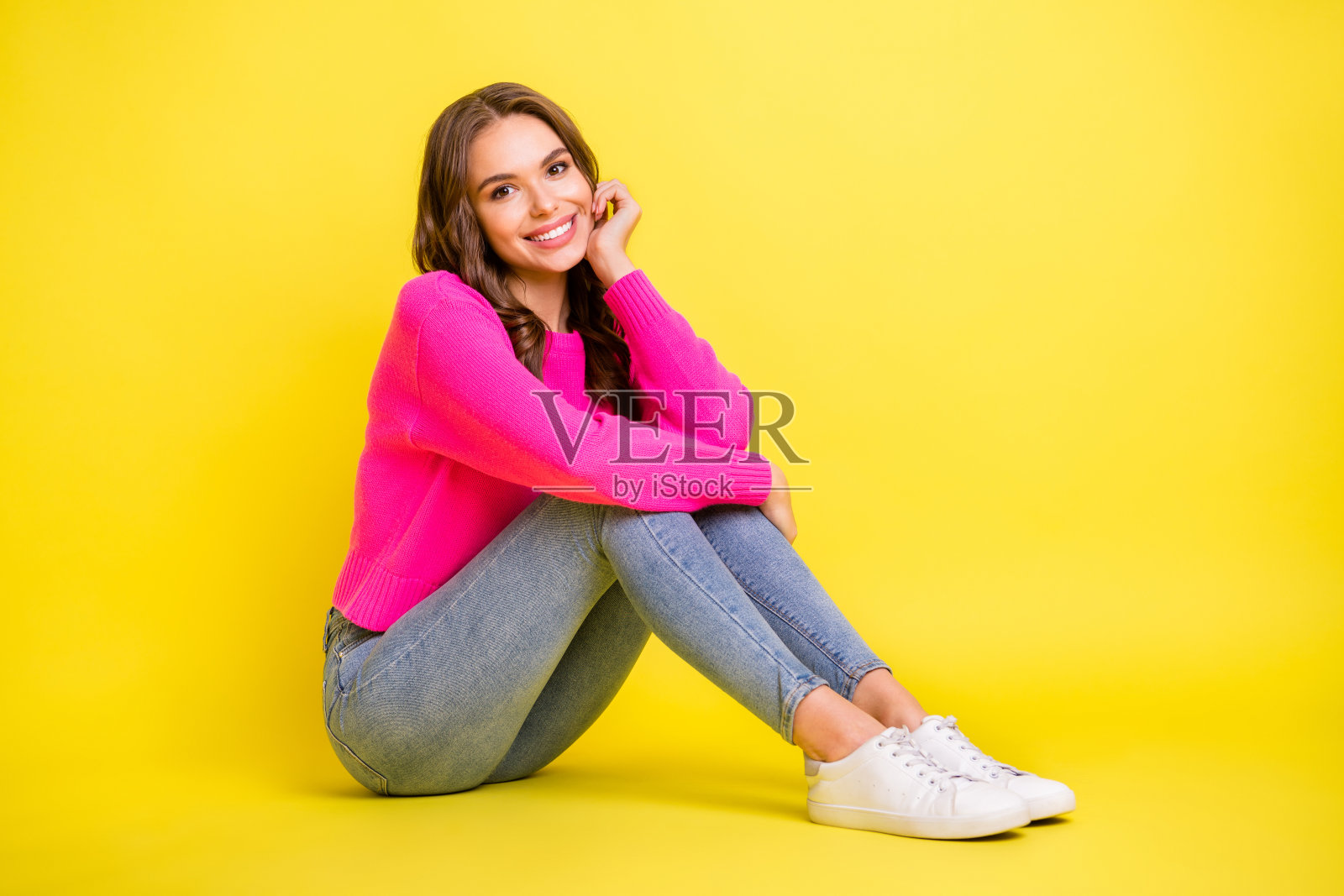 年轻漂亮女孩的全身侧面照片，开心地微笑，坐在地板上，背景为黄色。照片摄影图片