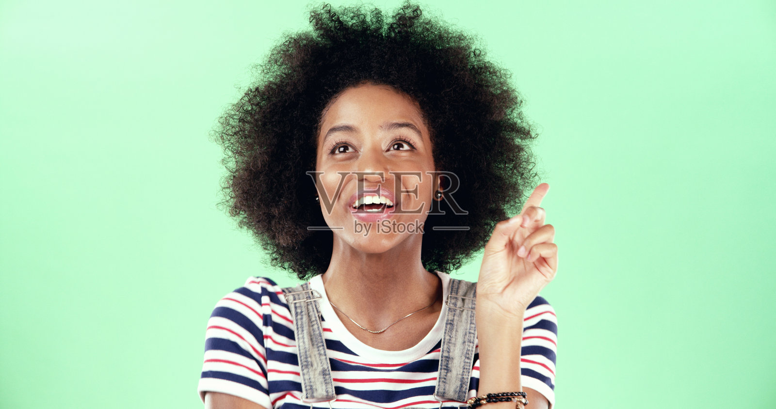 思考的黑人女性在工作室中指着想法，面带微笑。兴奋的女性在绿色背景下有了“啊哈”时刻，积极解决问题。照片摄影图片