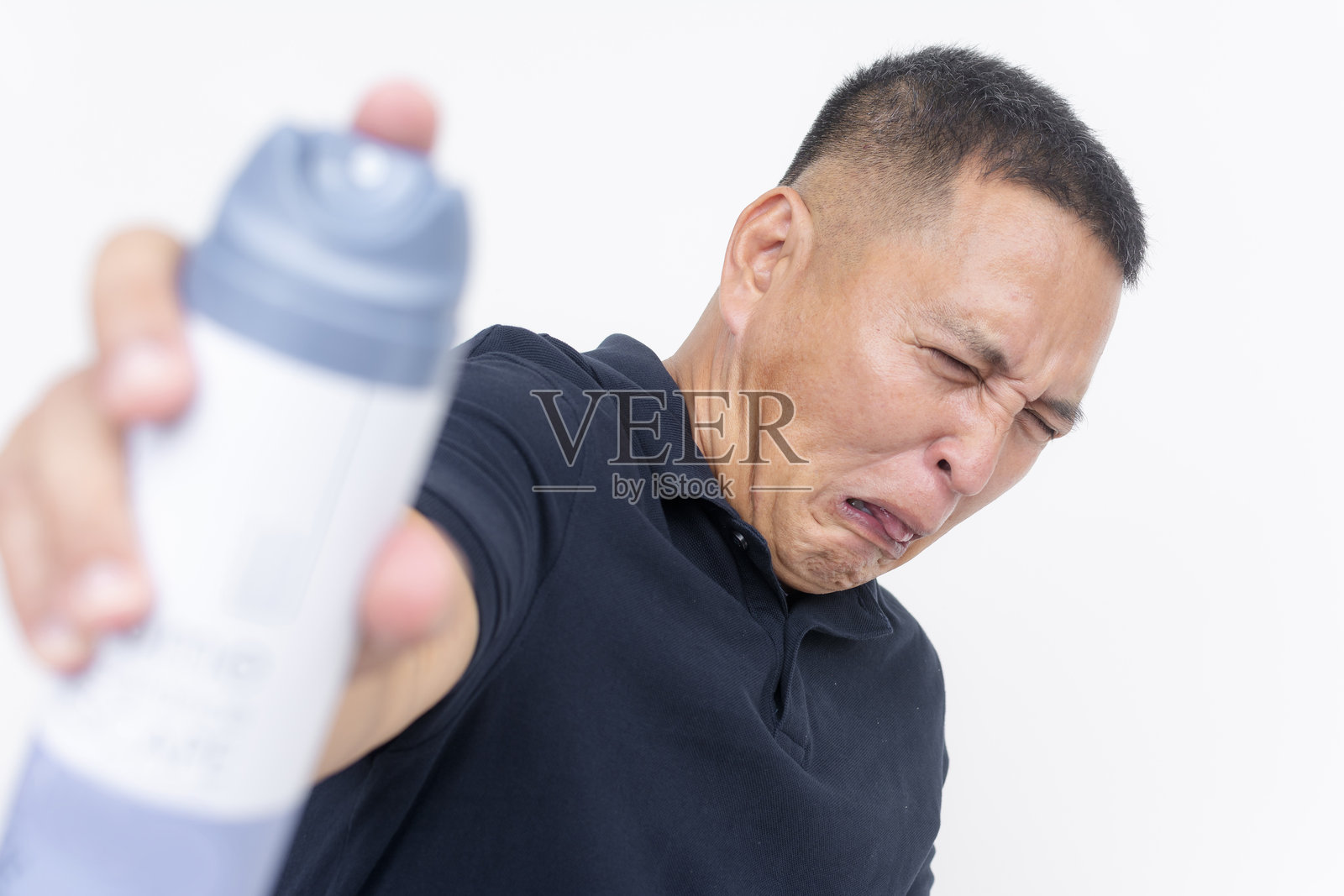 一名面露厌恶表情的男子正在使用空气清新剂喷雾来对抗难闻的气味，背景为白色。照片摄影图片
