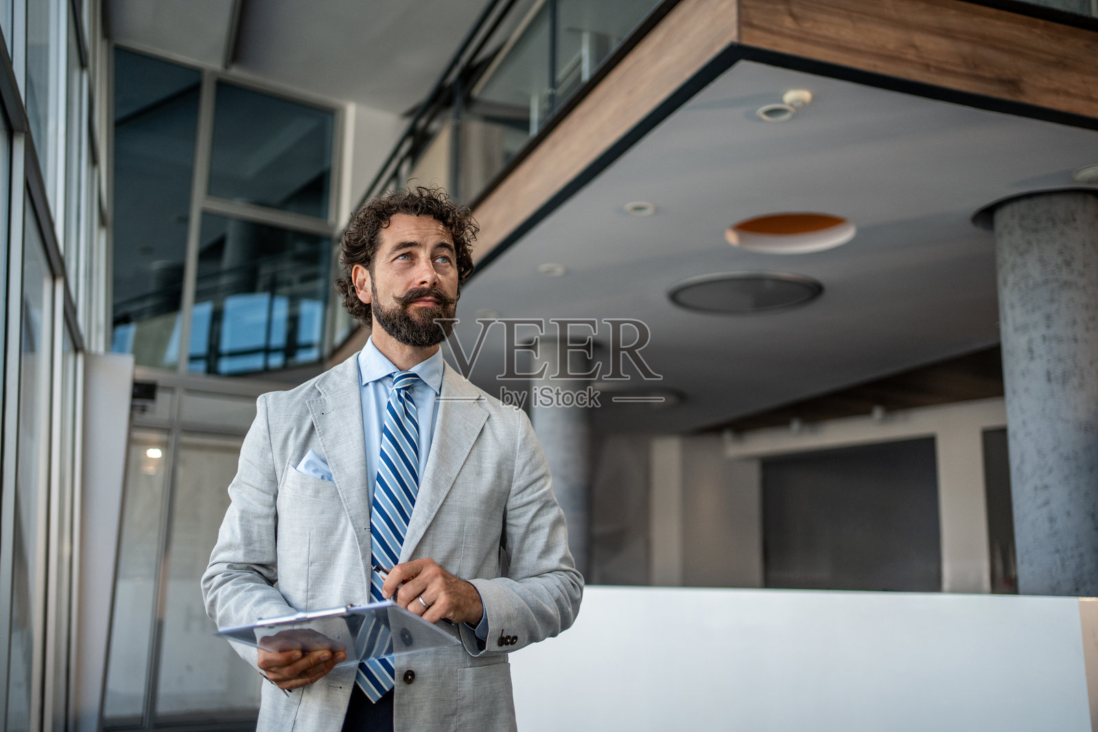 自信的商人手持夹板，在现代办公大楼中进行计划和思考照片摄影图片