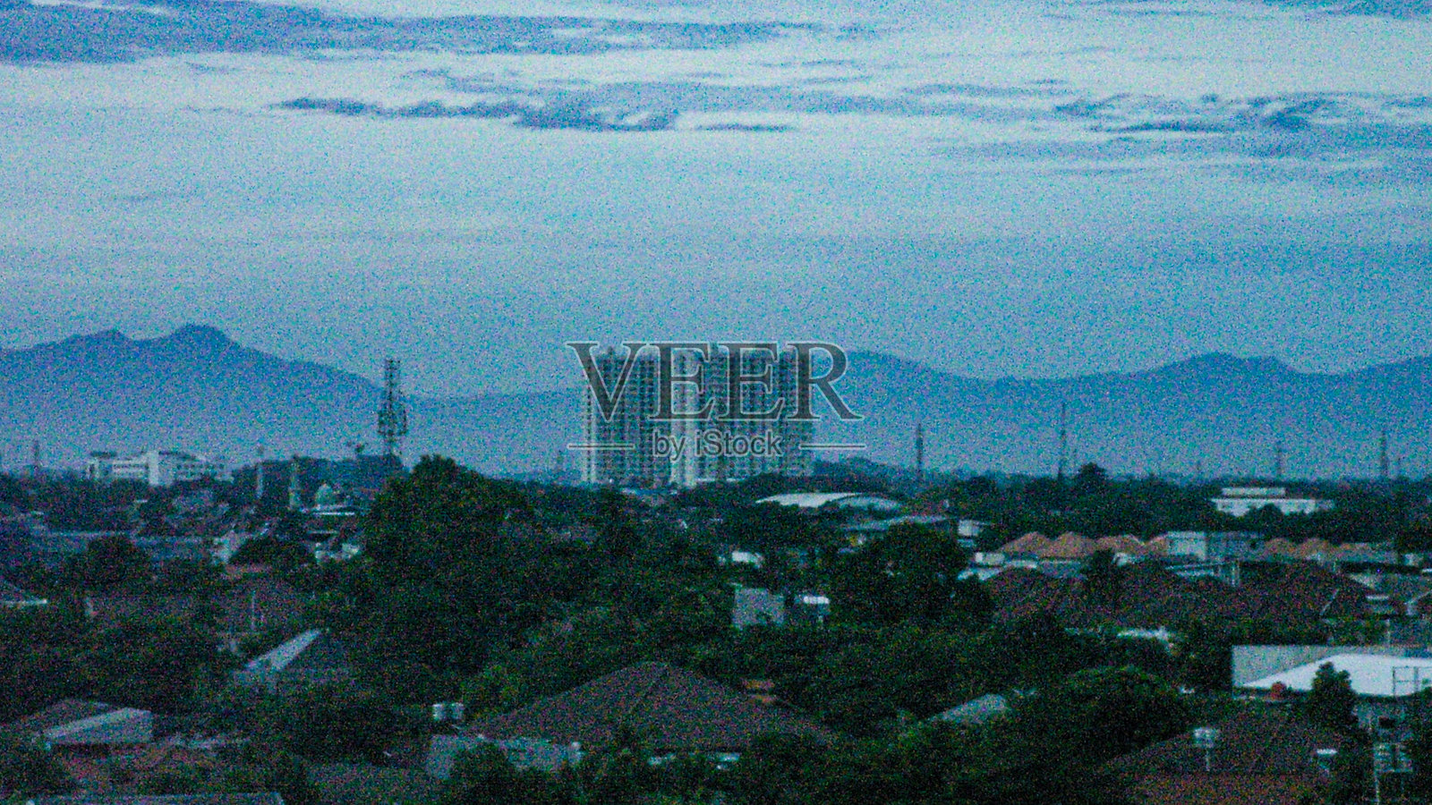 印度尼西亚黄昏时分，远景中的公寓楼与山脉背景。照片摄影图片