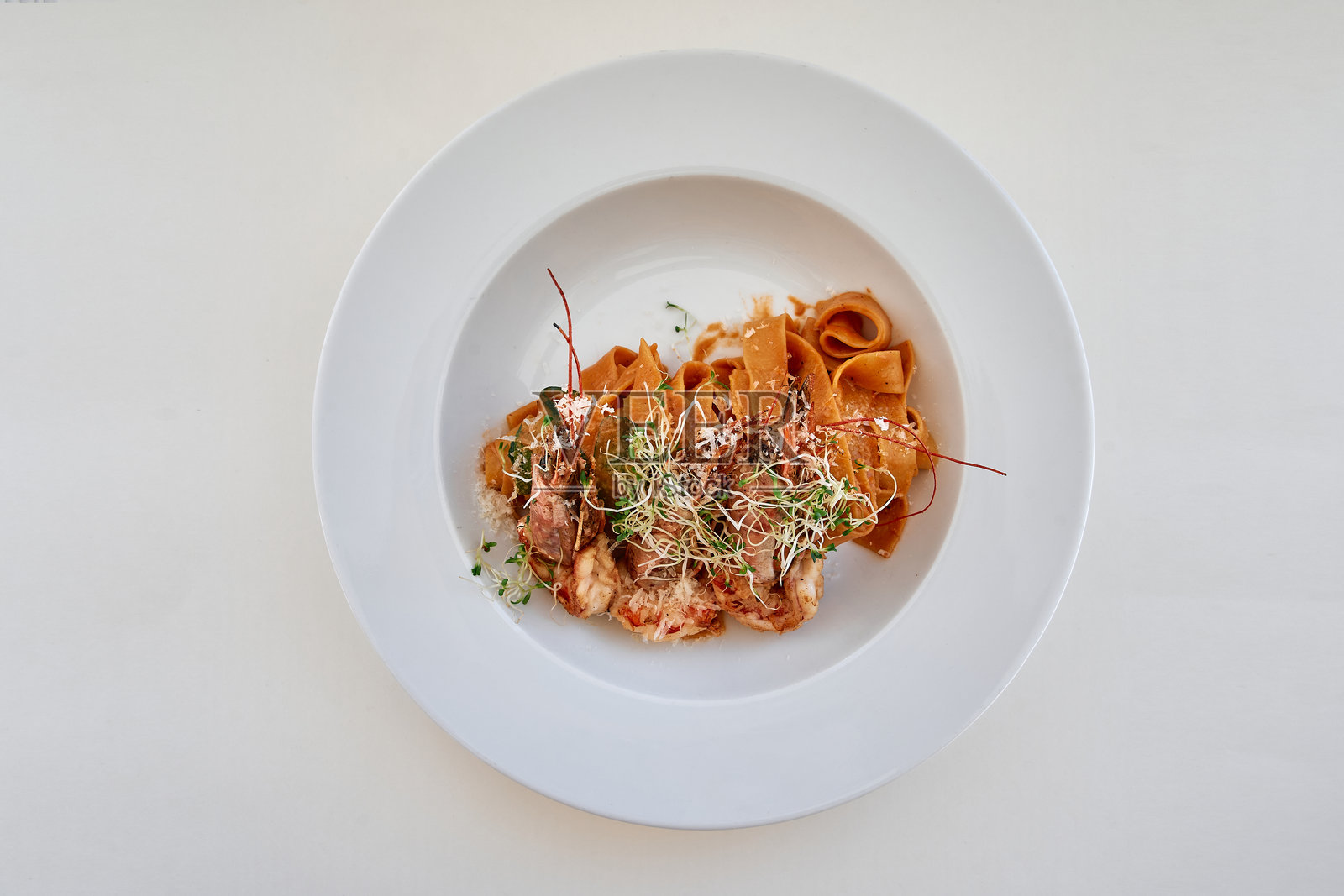 精致的意大利面菜肴，配有微型绿叶蔬菜和番茄酱，盛放在白色盘子上照片摄影图片