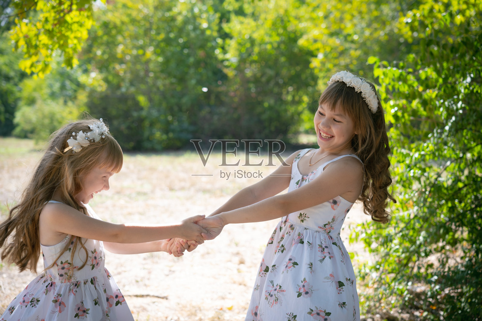 两个姐妹在大自然中做朋友。快乐女孩在绿叶树木旁的肖像。孩子们友好的关系。照片摄影图片