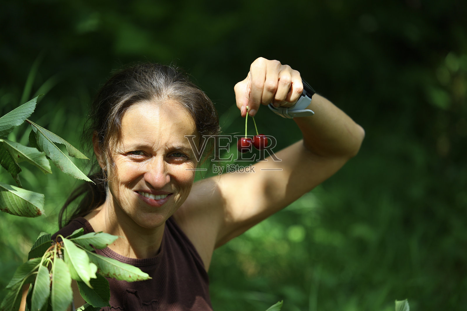 微笑的女性在绿色花园中手握两颗新鲜采摘的樱桃。照片摄影图片