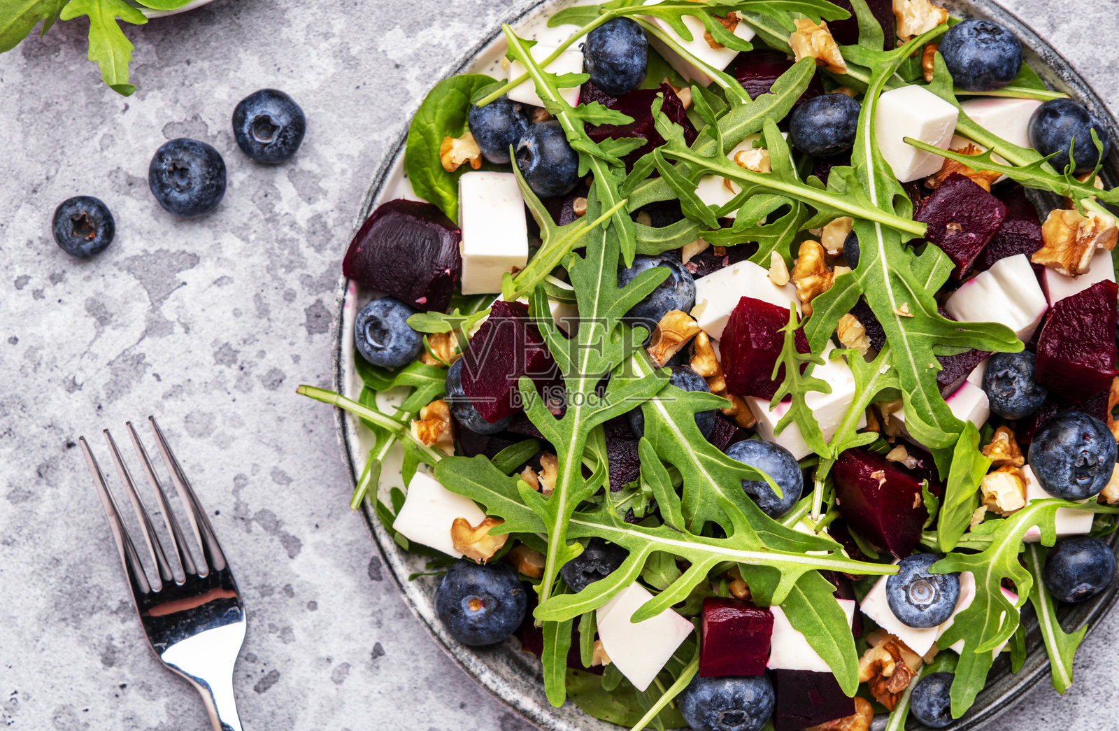 美味的沙拉，配有甜菜、蓝莓、奶酪、芝麻菜和核桃，灰色桌面背景，俯视图照片摄影图片