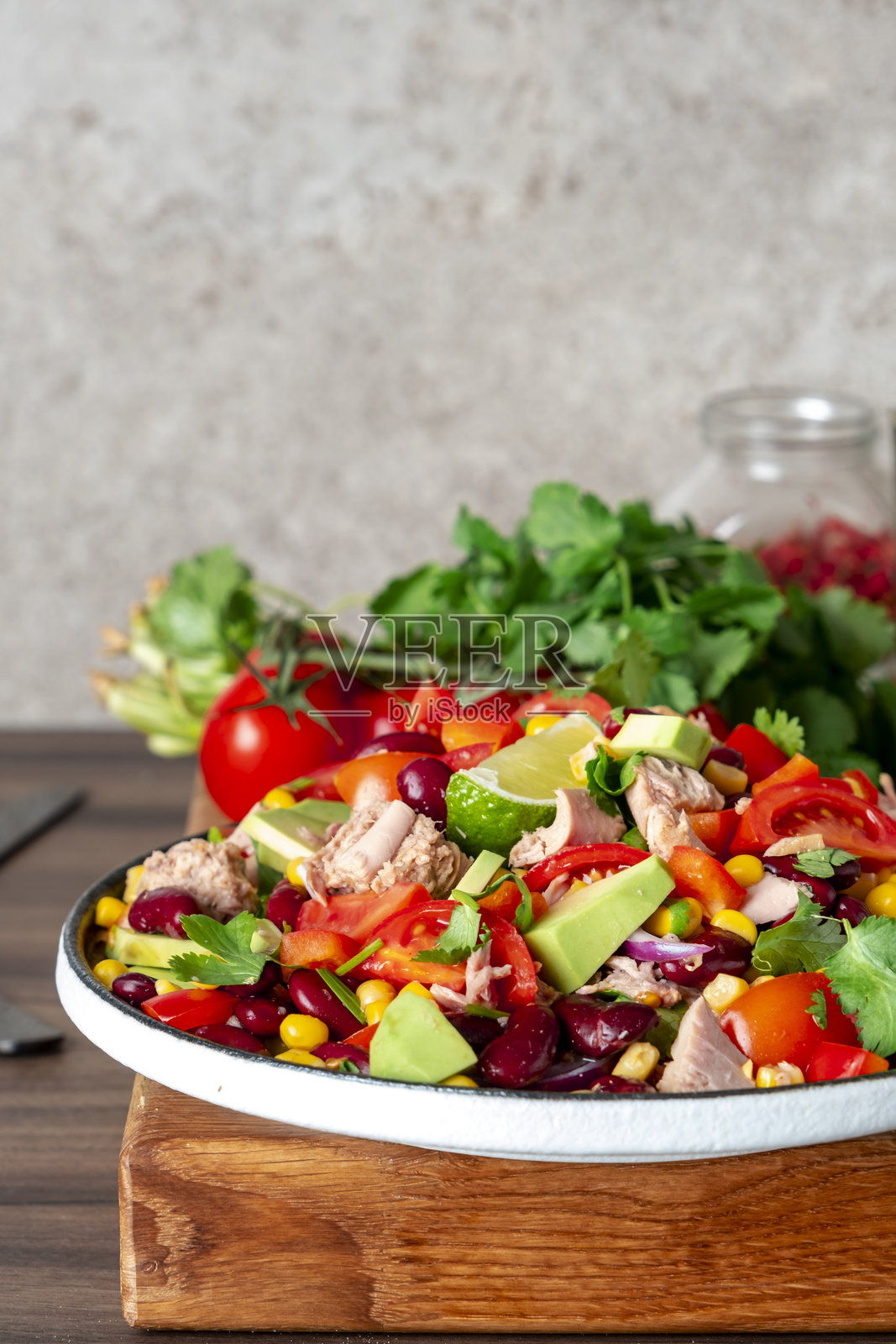 在厨房台面上准备美味的沙拉，沙拉中有金枪鱼、玉米、鳄梨、豆类、西红柿和香菜，旁边的木砧板上放着准备食材。照片摄影图片
