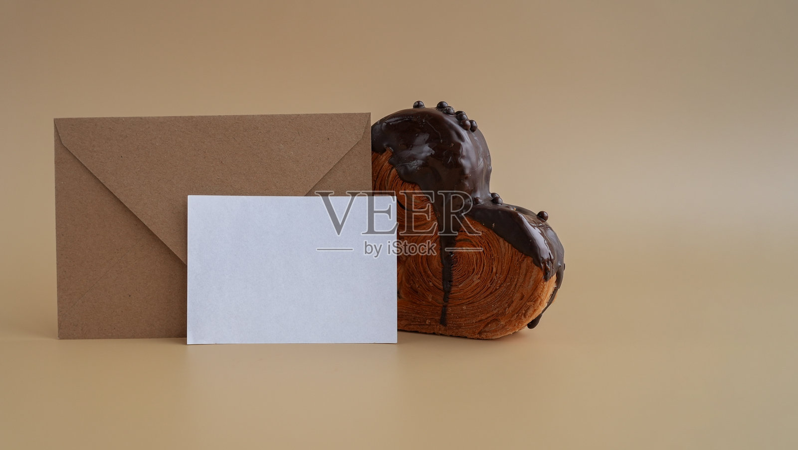 心形黑巧克力可颂在米色背景上的纸质便条卡模板，留有空白空间。新潮的酥皮甜点烘焙。奶油面团照片摄影图片