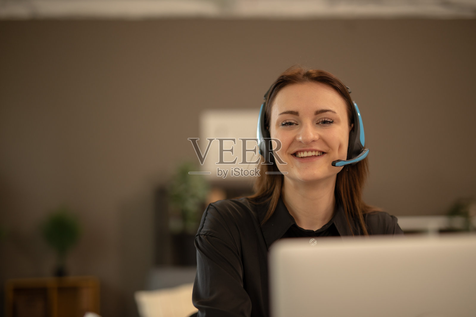 年轻女性在家工作，佩戴耳机，微笑着看着笔记本电脑。照片摄影图片