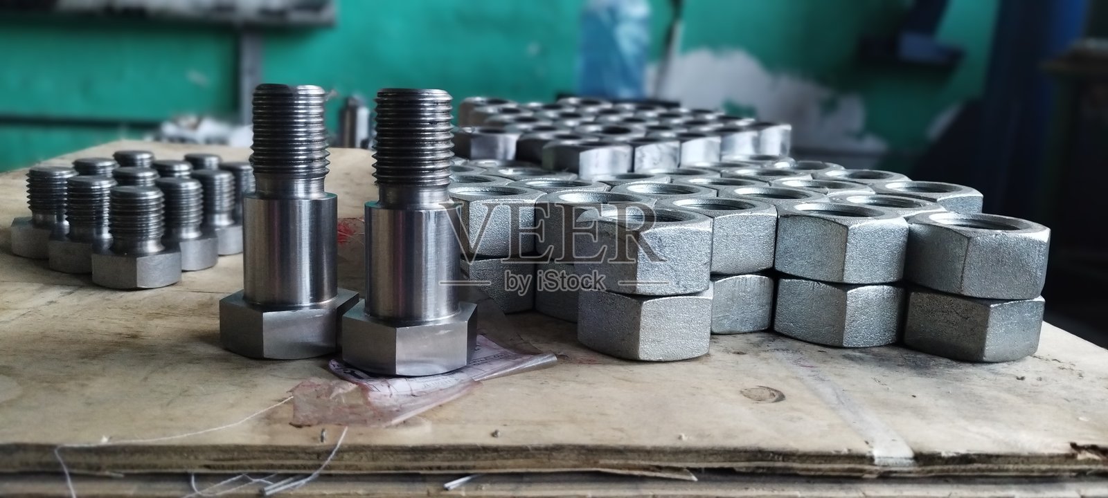 新型金属螺栓和螺母的特写。钢制螺栓和螺母。工业紧固件展示在木质表面上，背景为模糊的车间。带法兰的钢制六角螺母。机械工程。照片摄影图片