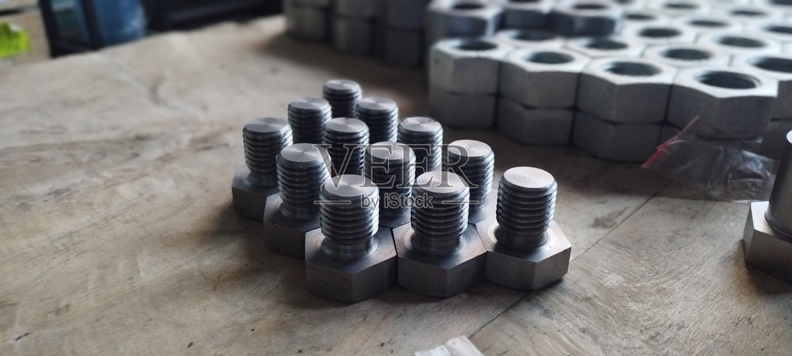 一组新金属螺栓的特写。六角头螺栓在焦点中，螺母在背景中。工业紧固件放置在木质表面上。选择性对焦，背景模糊。照片摄影图片