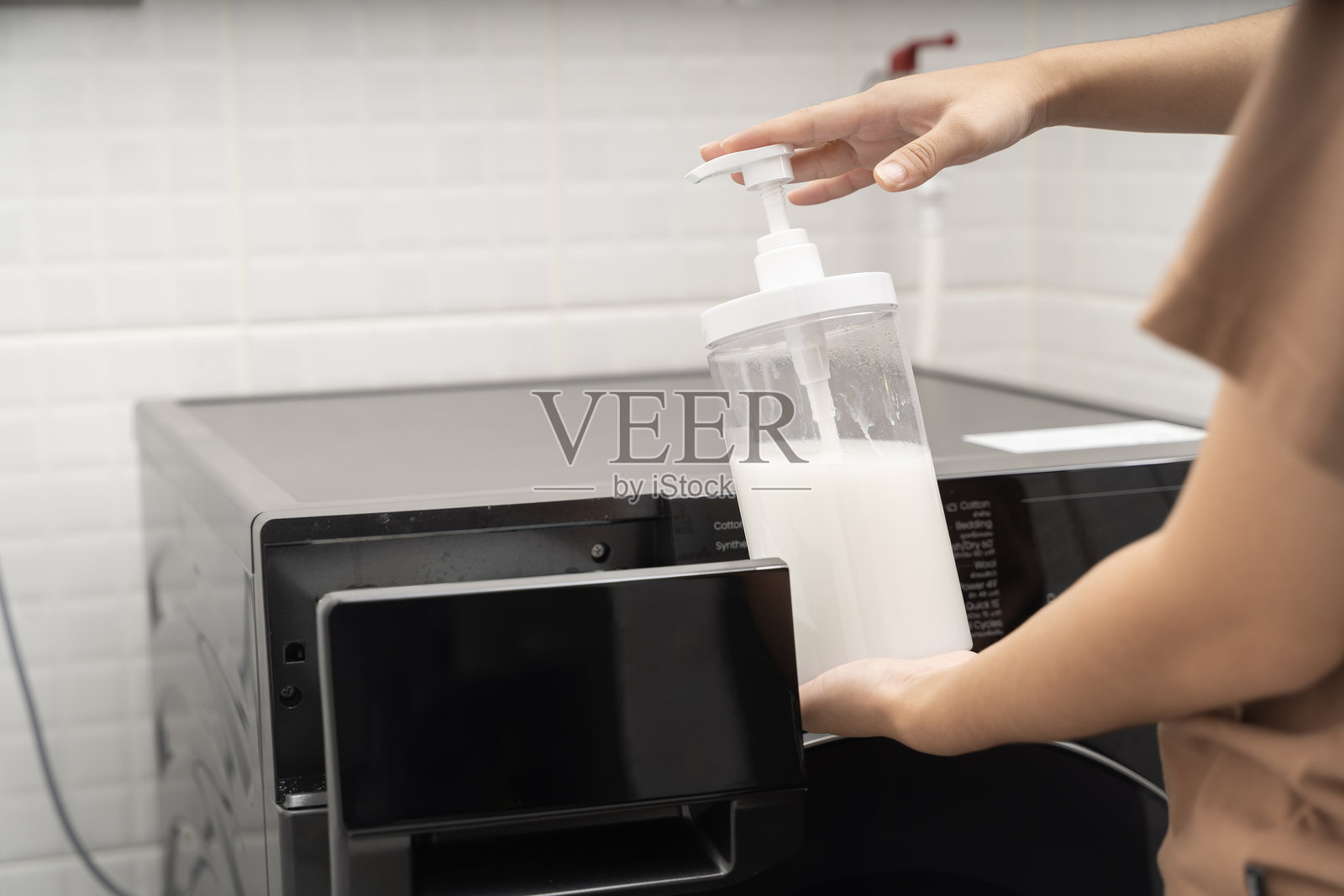 手握白色液体洗涤剂瓶，带泵，悬在洗衣机上，用于家庭清洁洗衣工作照片摄影图片