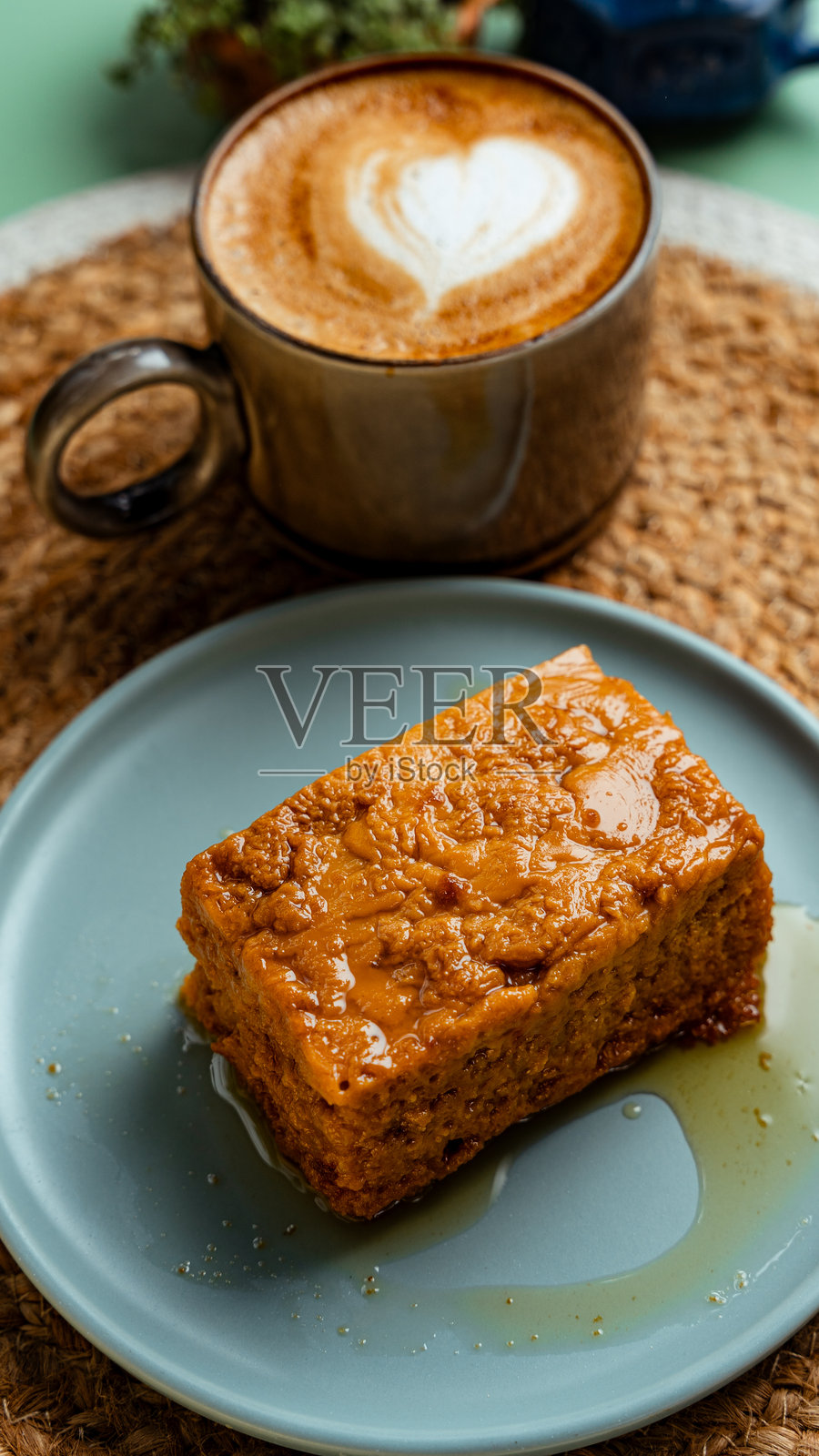 美味的蛋糕切片，上面有焦糖浇头，旁边是一杯带有拉花心形图案的卡布奇诺。照片摄影图片