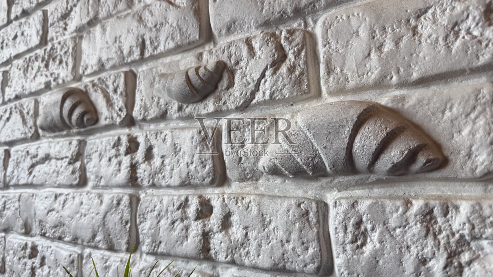 艺术装饰的可颂面包细节雕刻在白色纹理的仿砖墙上。石膏元素与墙面融为一体，创造性地结合了烹饪和建筑美学。照片摄影图片