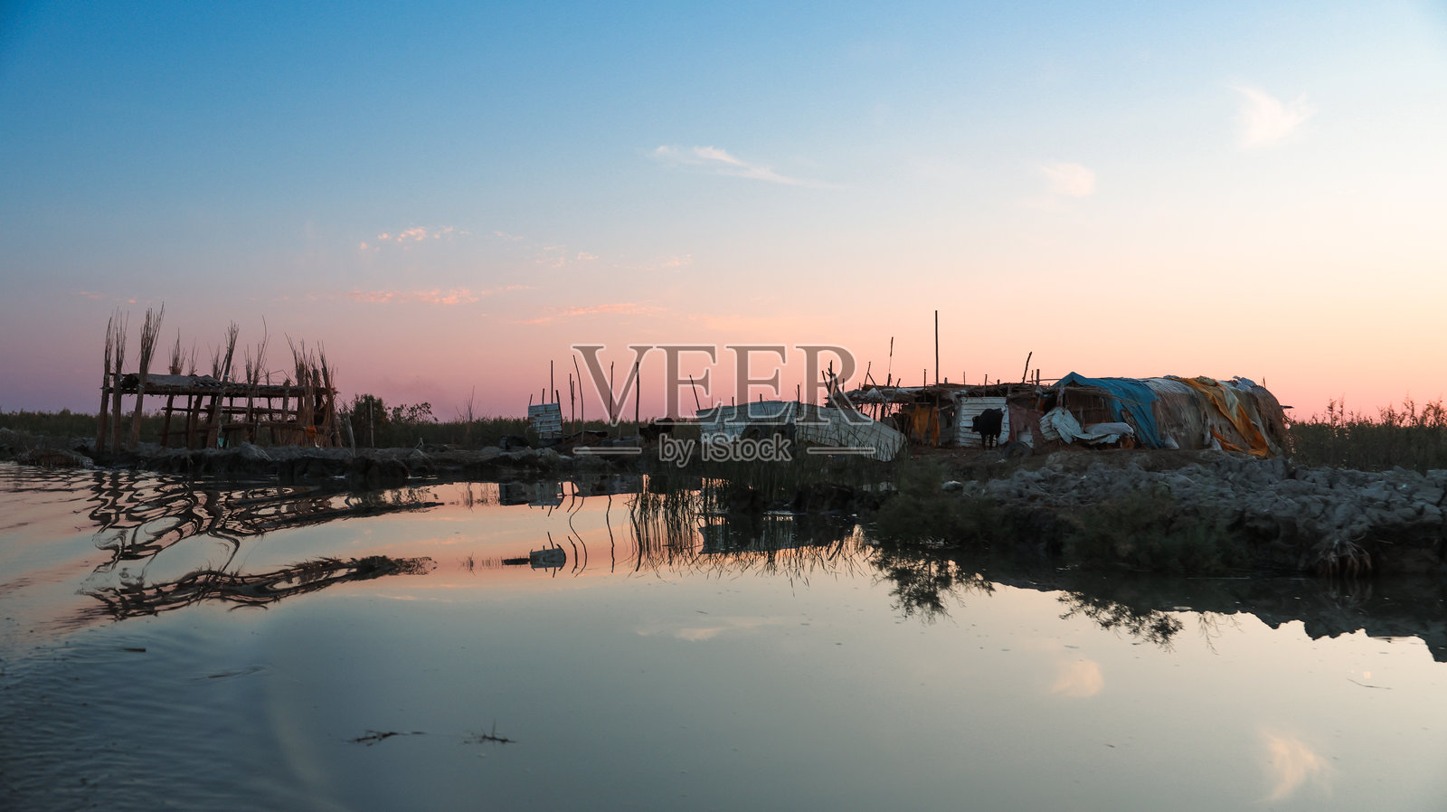黄昏时分的美索不达米亚沼泽地，展示传统小屋和宁静的水面倒影照片摄影图片